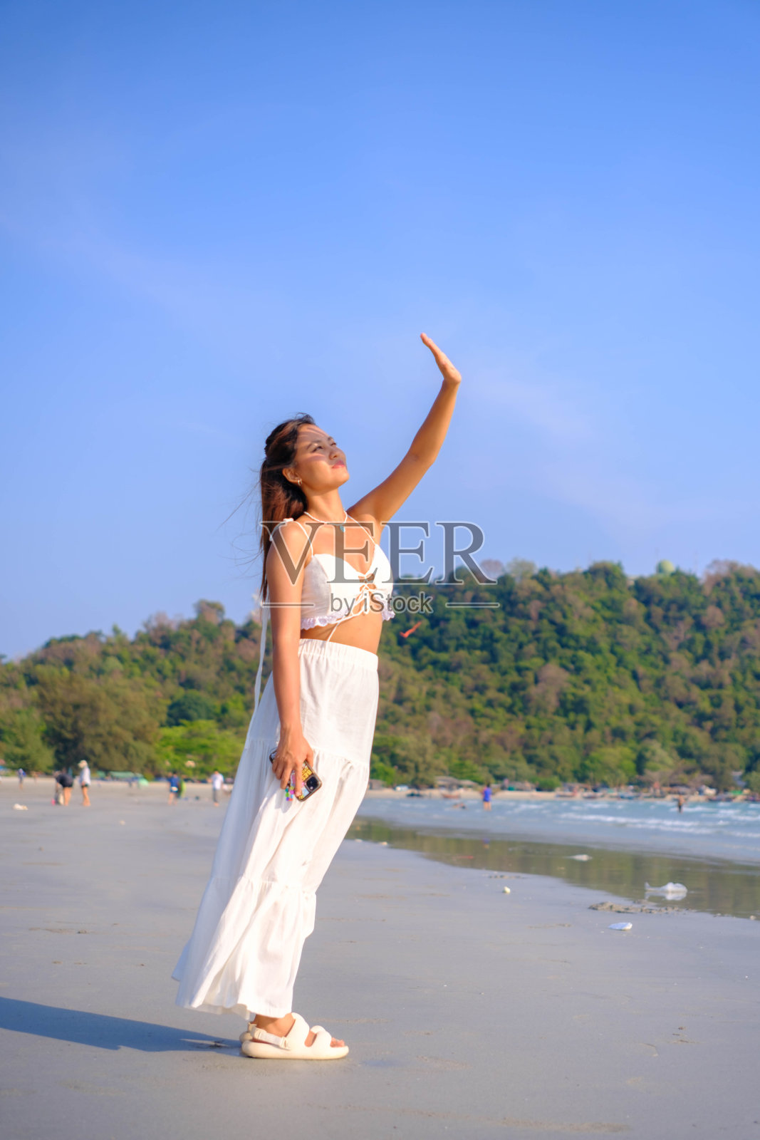 美丽的亚洲女人穿着白色的裙子站在海边享受阳光。照片摄影图片
