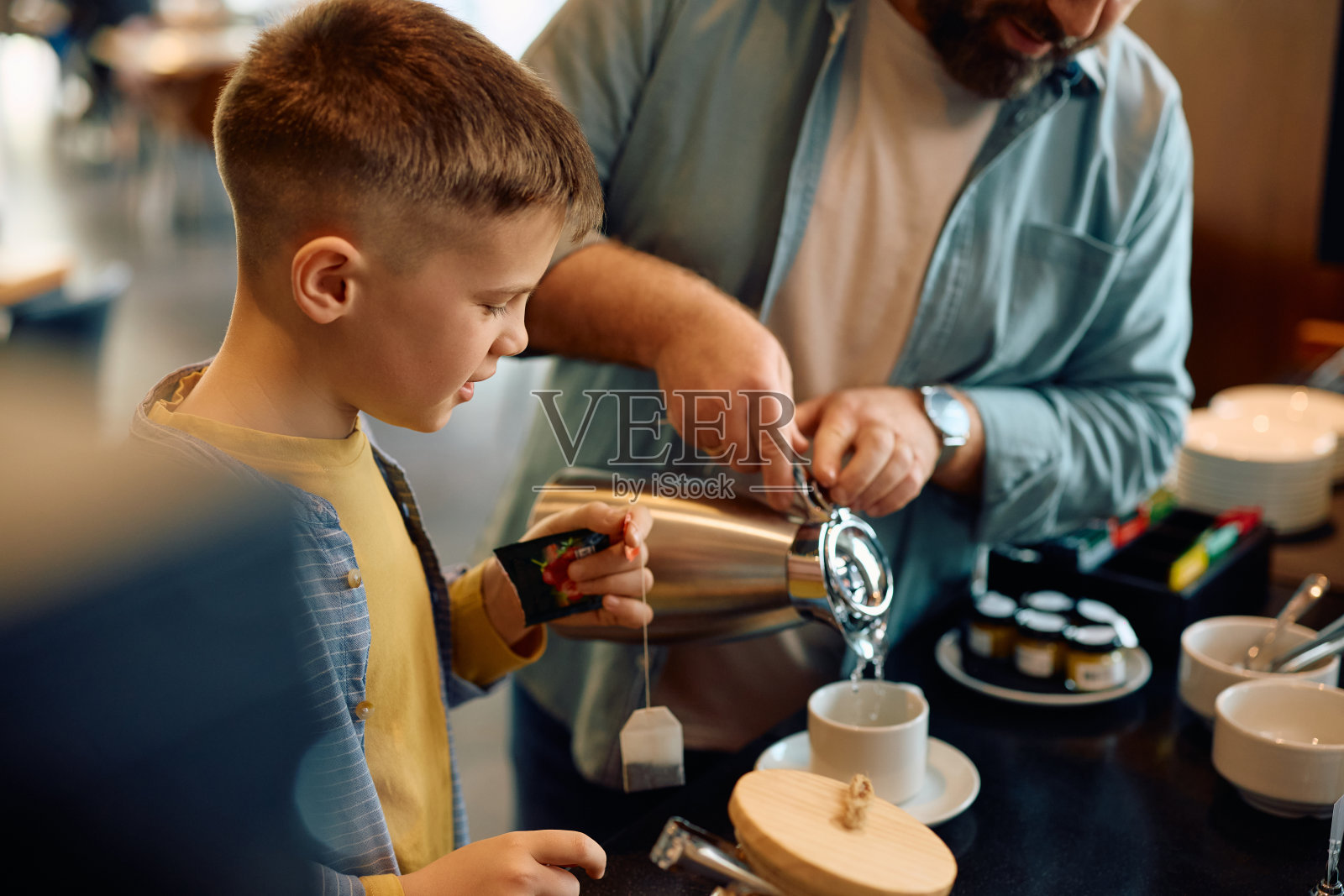 微笑的男孩和他的父亲在酒店餐厅边泡茶边吃早餐。照片摄影图片