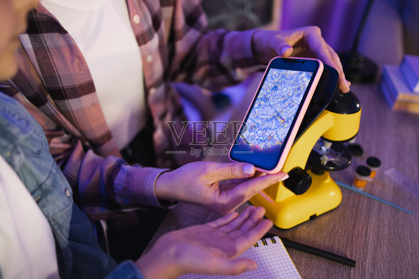 两个女人坐在桌边，在家里用手机做显微照片。照片摄影图片