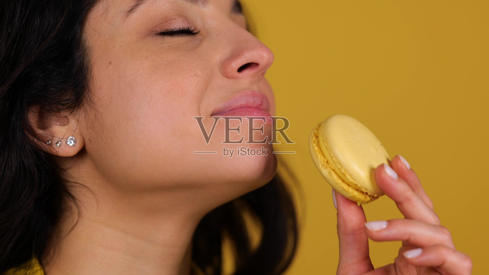 年轻的女士一边吃马卡龙一边享受，孤立在黄色背景上，复制空间，近距离拍摄。甜食概念。实时照片摄影图片