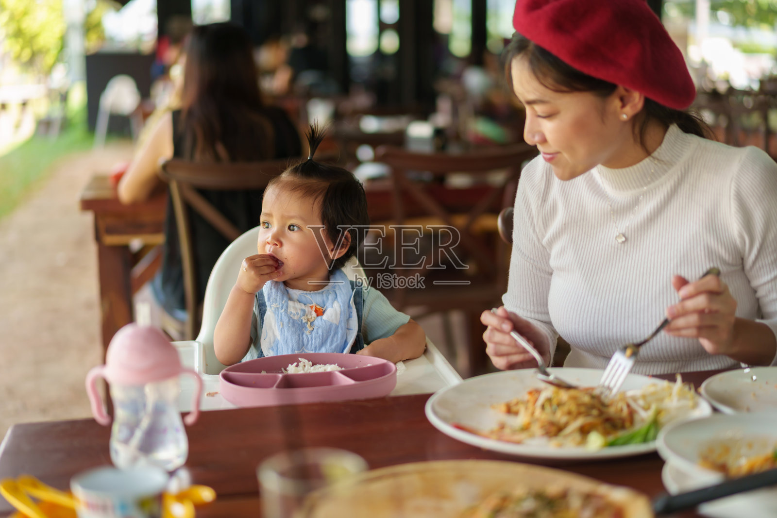 母亲带着蹒跚学步的小女孩在餐厅里用自己喂养的BLW或婴儿在高脚椅上断奶照片摄影图片