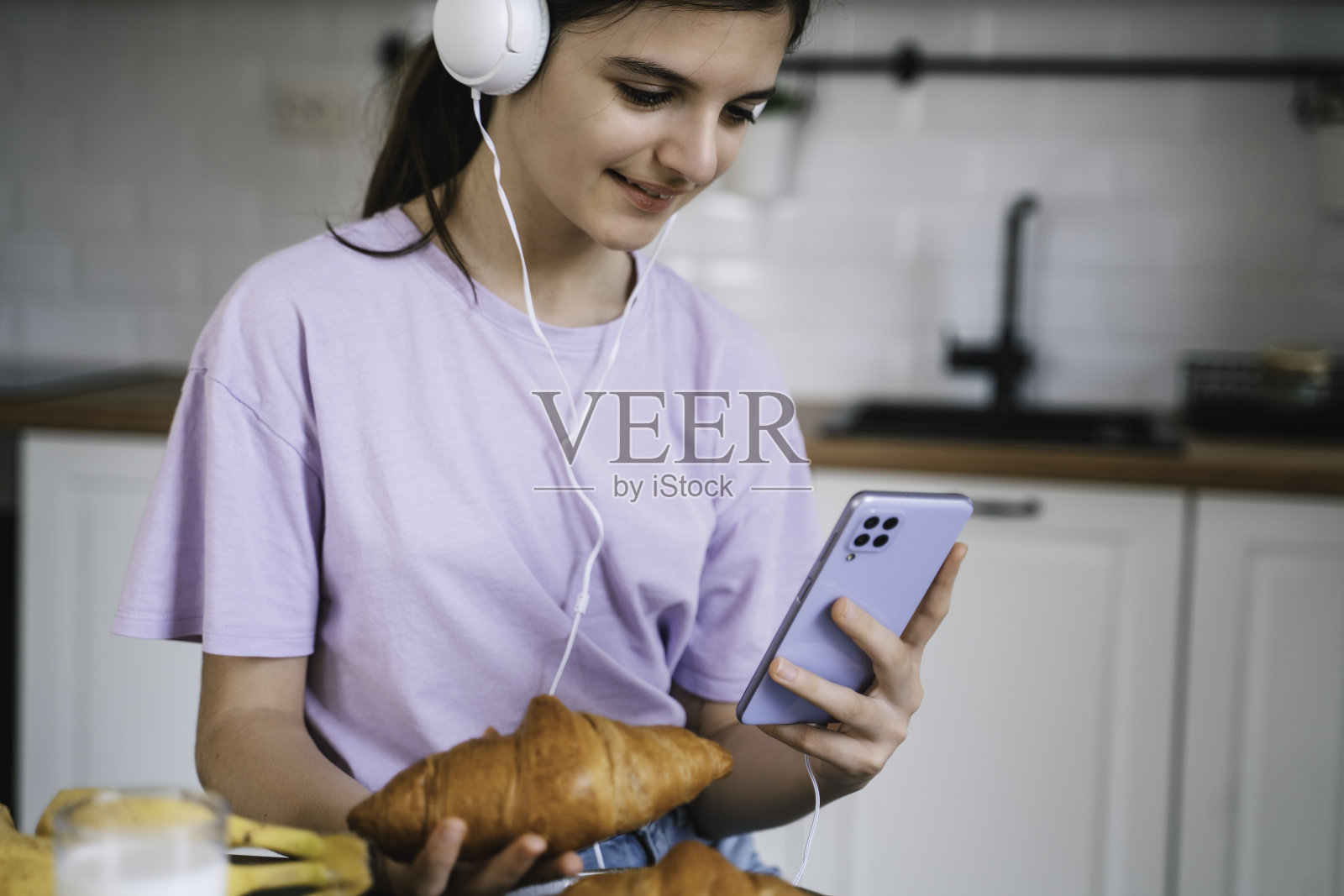 美丽的女孩在厨房吃早餐时使用手机。照片摄影图片