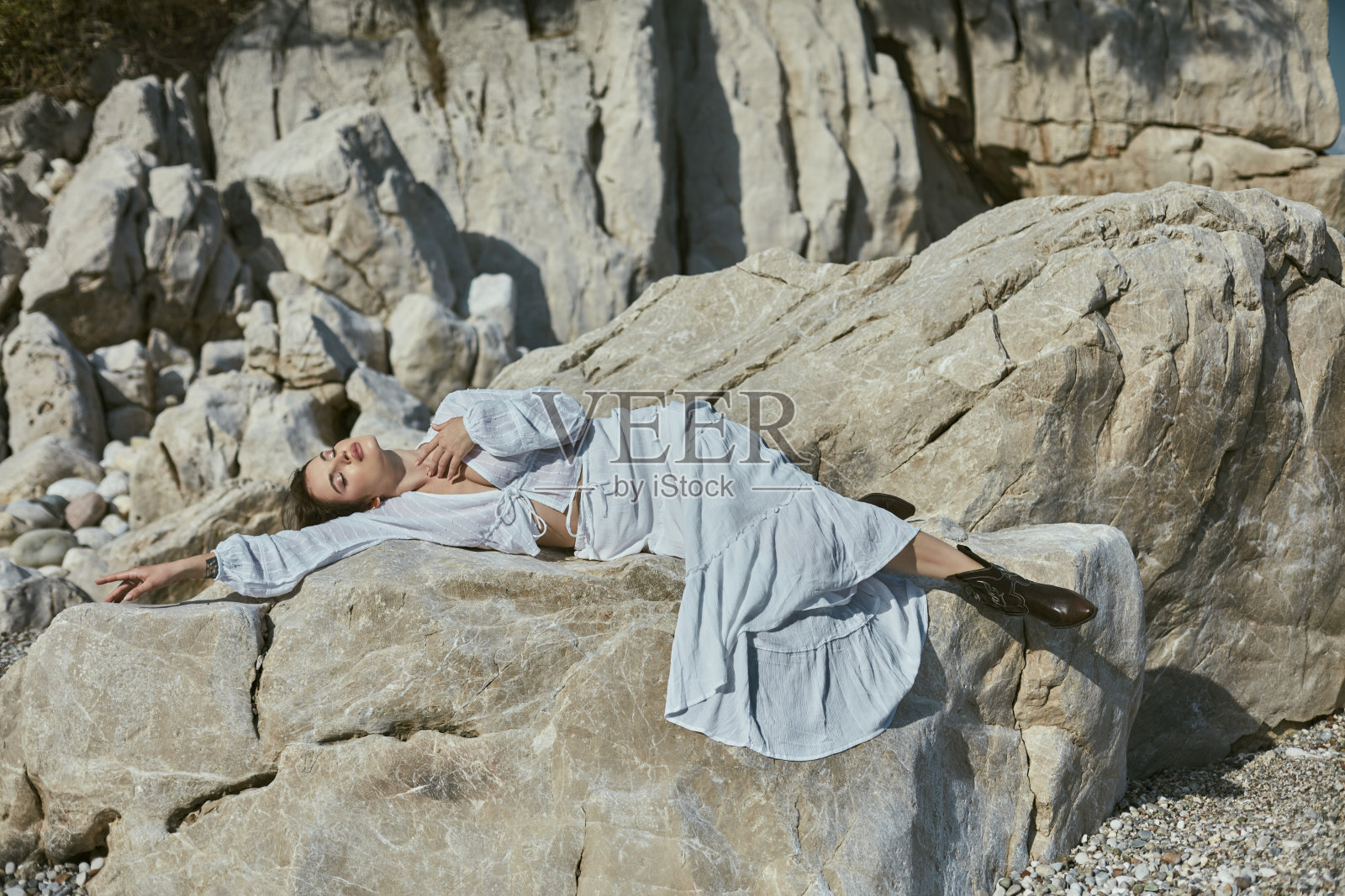 美丽的女人躺在沙滩上的岩石上，享受着美好的天气，晒日光浴。照片摄影图片