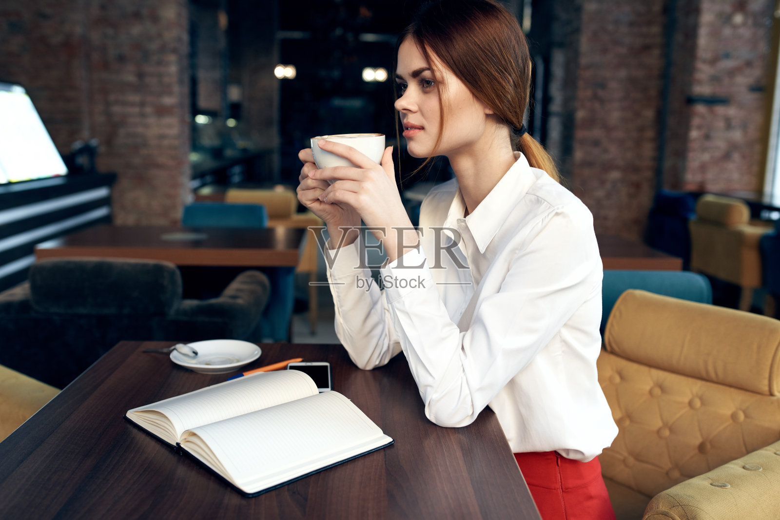 美女端着杯子坐在咖啡馆的桌子旁，预订了餐厅照片摄影图片