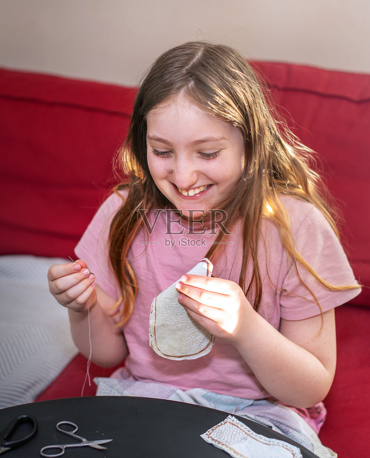 咯咯笑着的10岁女孩正在学习用布料缝制毛绒玩具。照片摄影图片