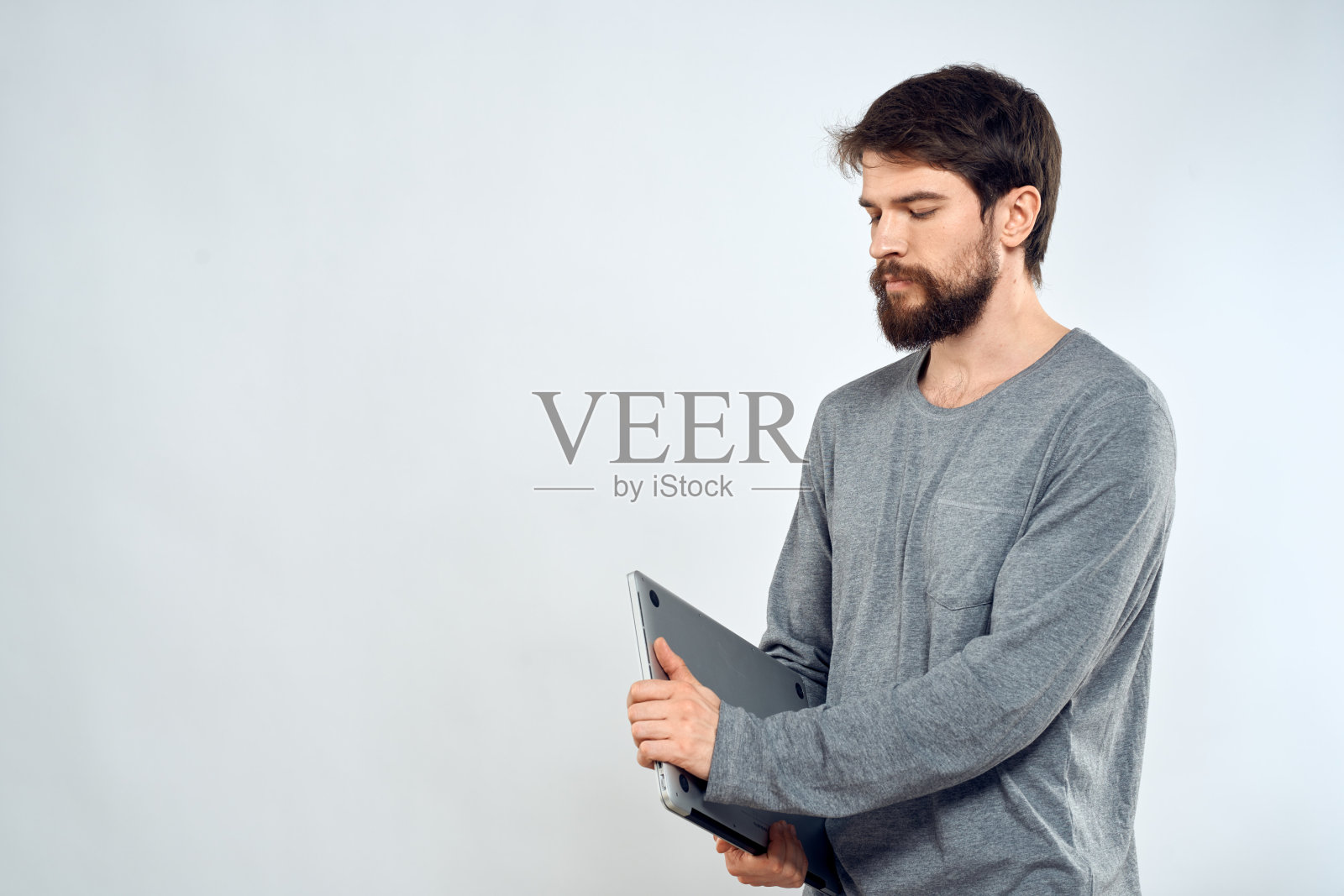 一个穿着灰色毛衣的男人拿着笔记本电脑，手握生活科技通讯互联网工作照片摄影图片