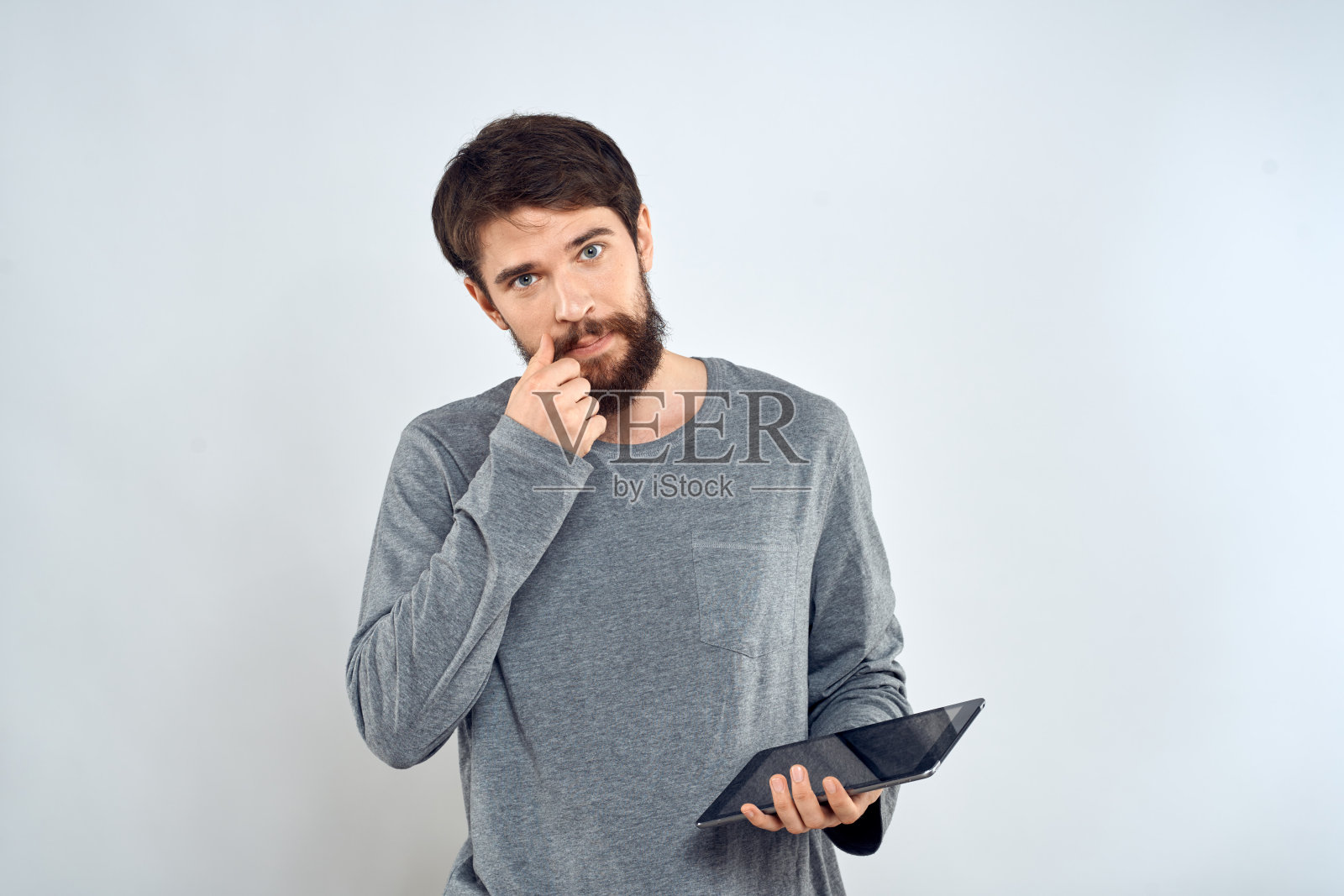 一个留着胡子的男人，手里拿着平板电脑，灰色夹克，科技互联网，浅色背景照片摄影图片