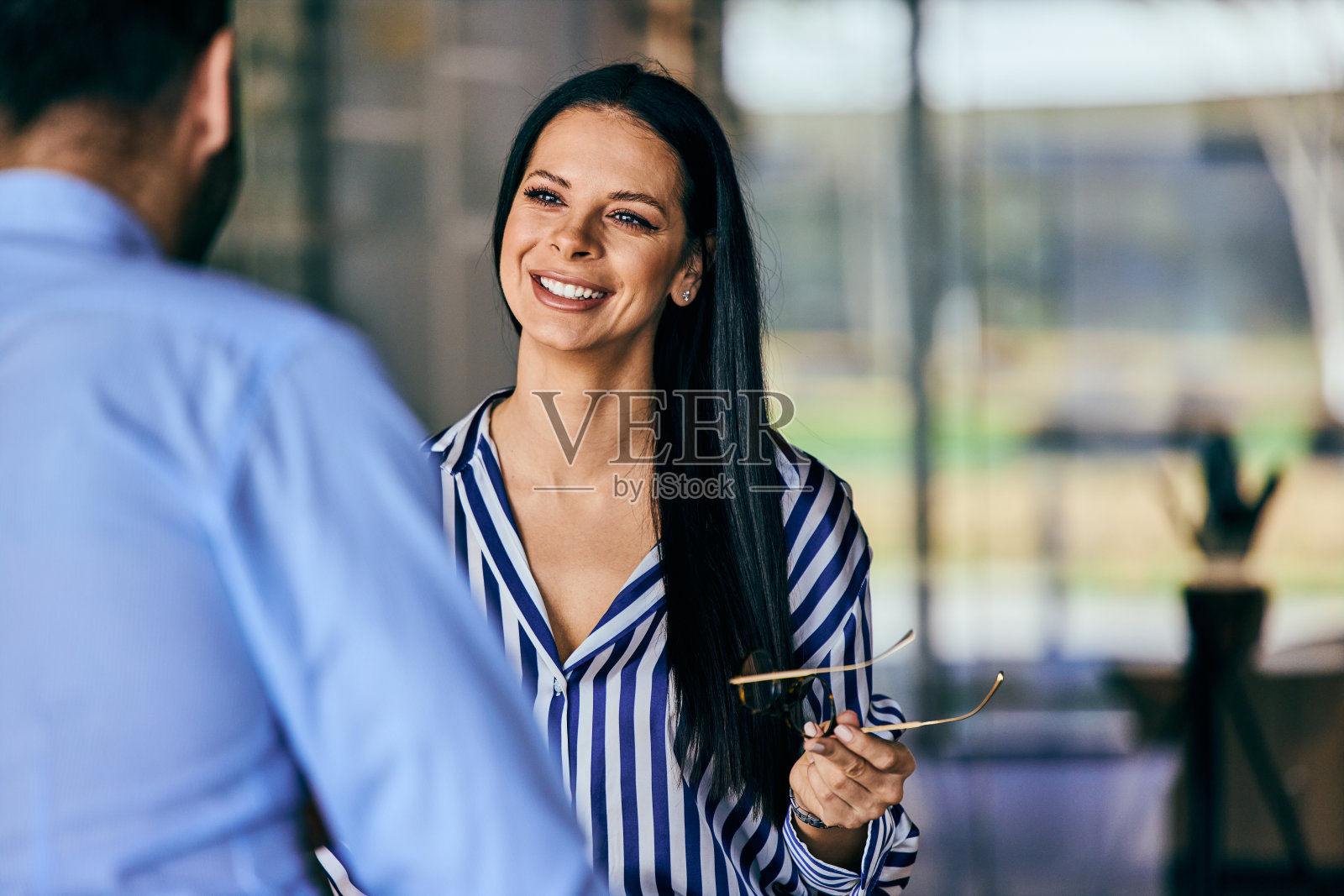 一个戴着眼镜的微笑的女人在办公室和她的同事交谈。照片摄影图片