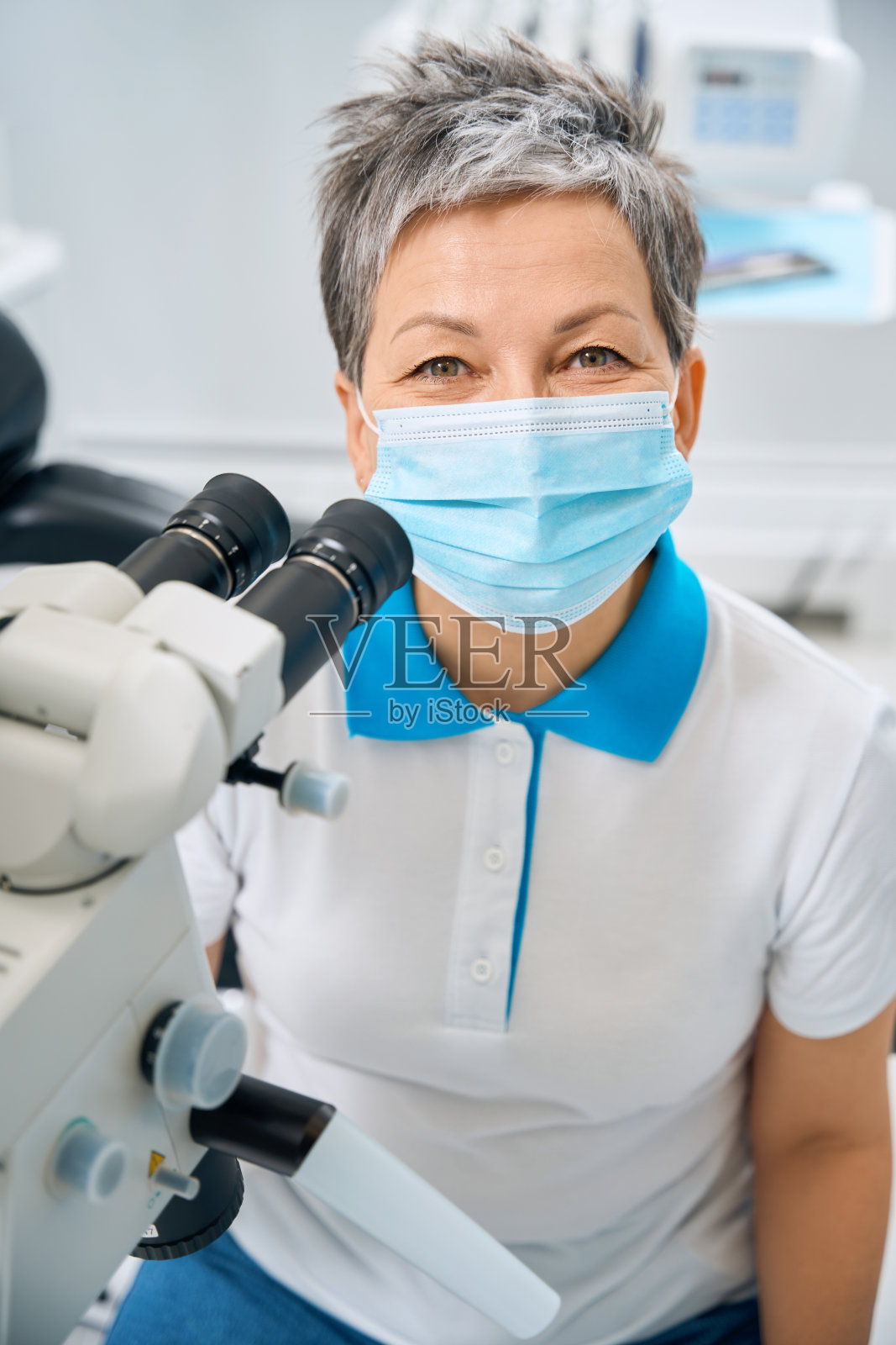 阳性的女牙科医生坐在她的办公室里靠近显微镜照片摄影图片