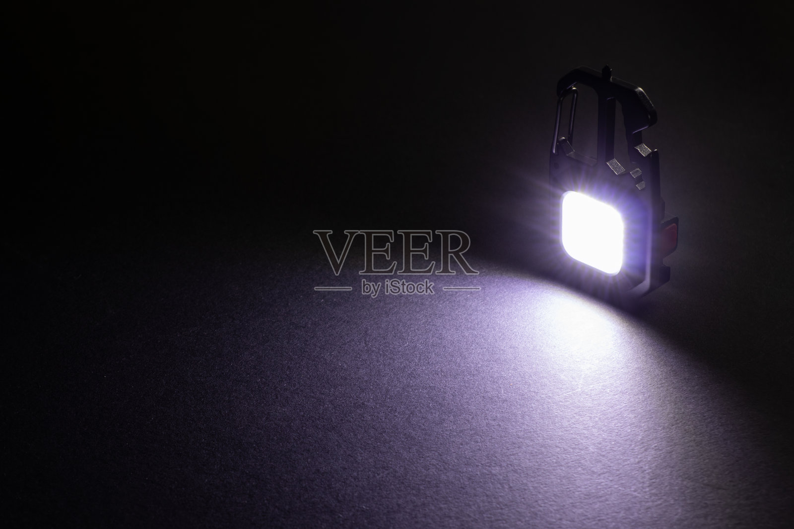 LED手电筒钥匙扣和黑暗中的一束光。一个现代的led灯，明亮的投影在黑暗的桌子。照片摄影图片