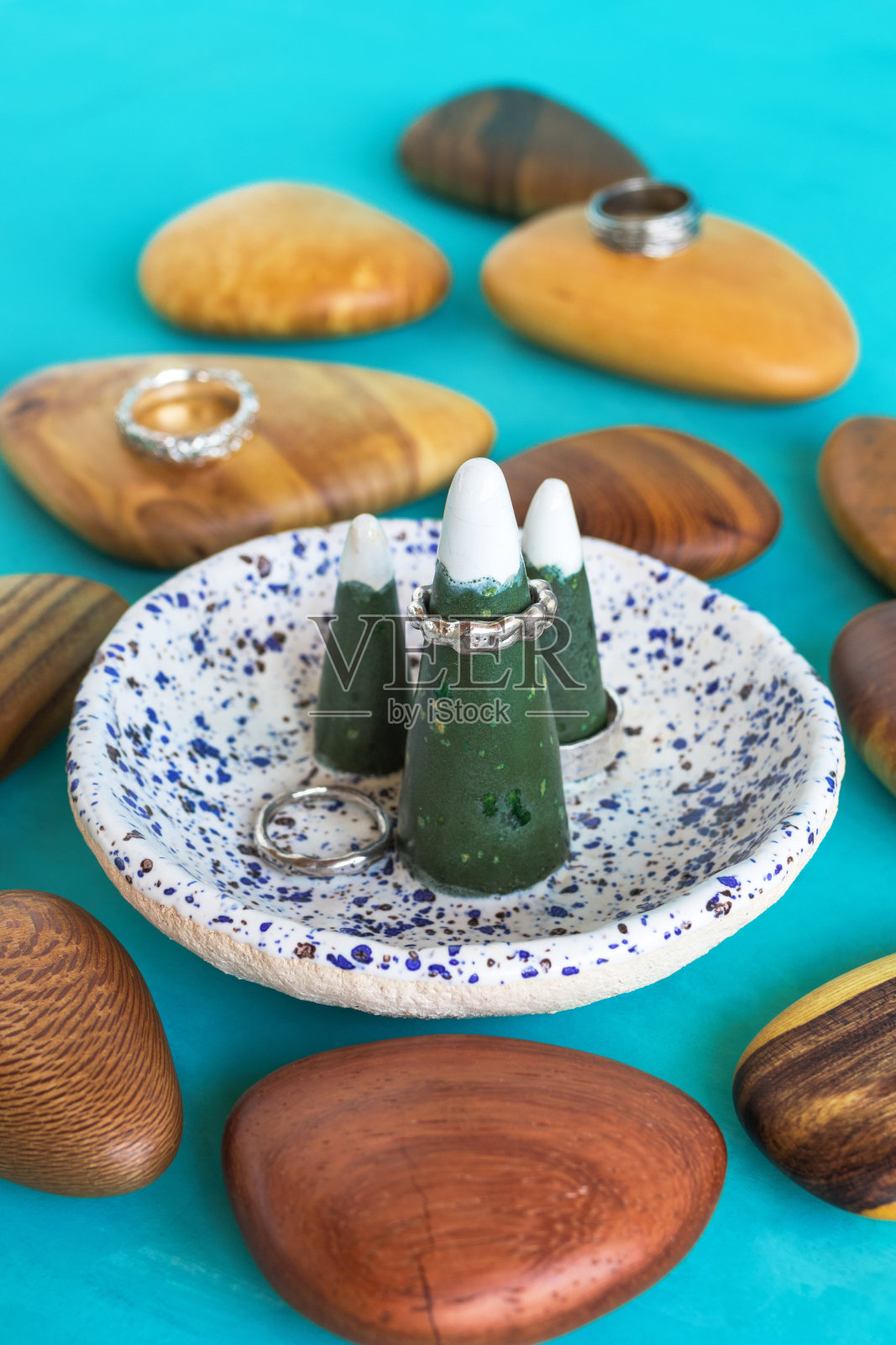 手工银戒指上的陶瓷环架上的蓝色背景与木制物品。手工珍贵物品。珠宝配饰。照片摄影图片