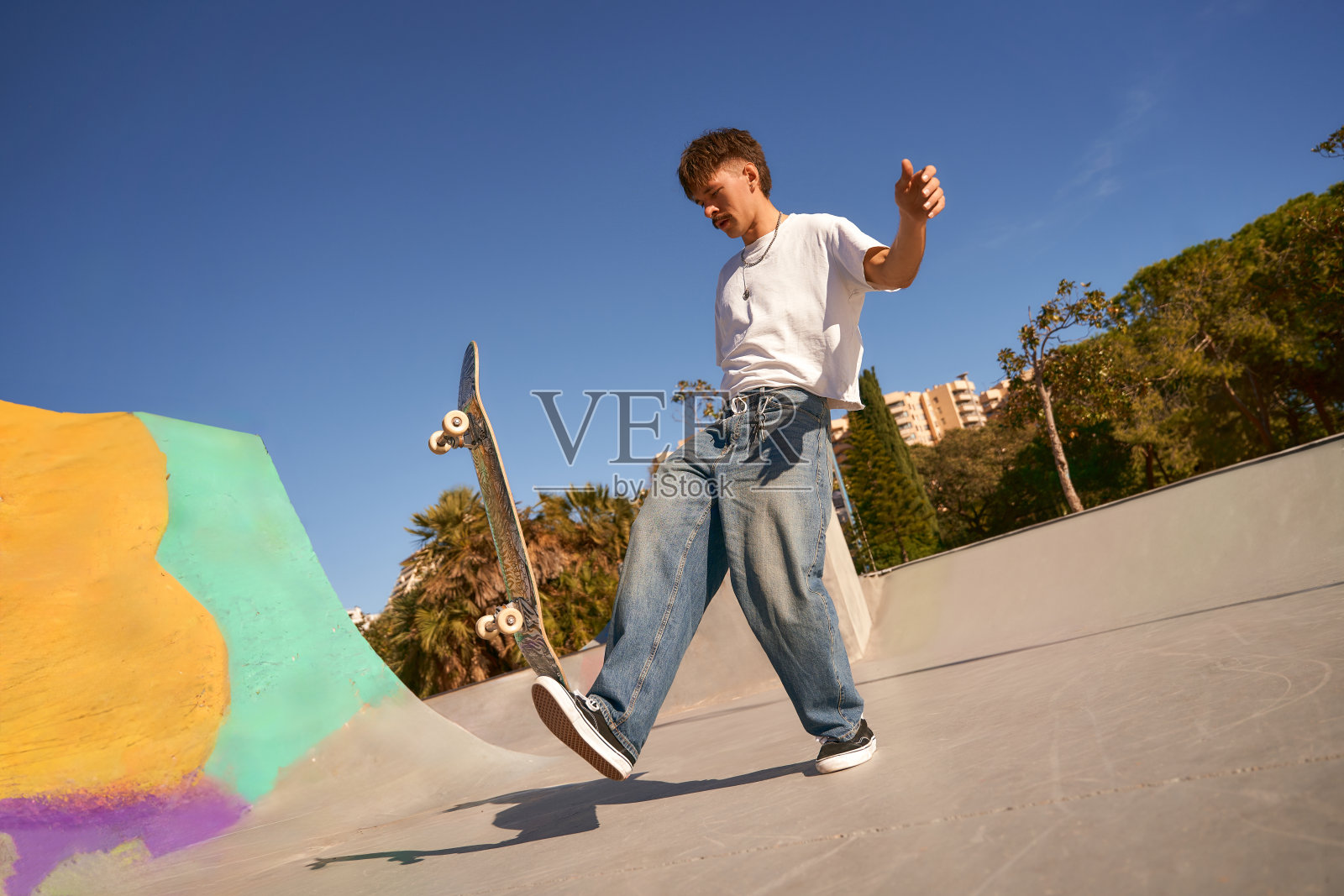 在一个阳光明媚的日子里，一个兴奋的年轻人在滑板公园玩滑板。极限运动概念照片摄影图片