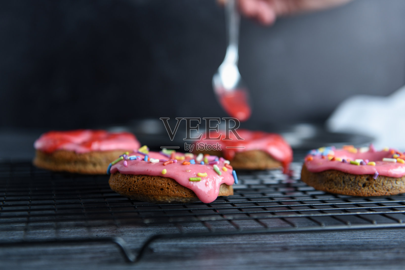 用勺子将新鲜的釉料淋在刚烤好的甜甜圈上的手照片摄影图片