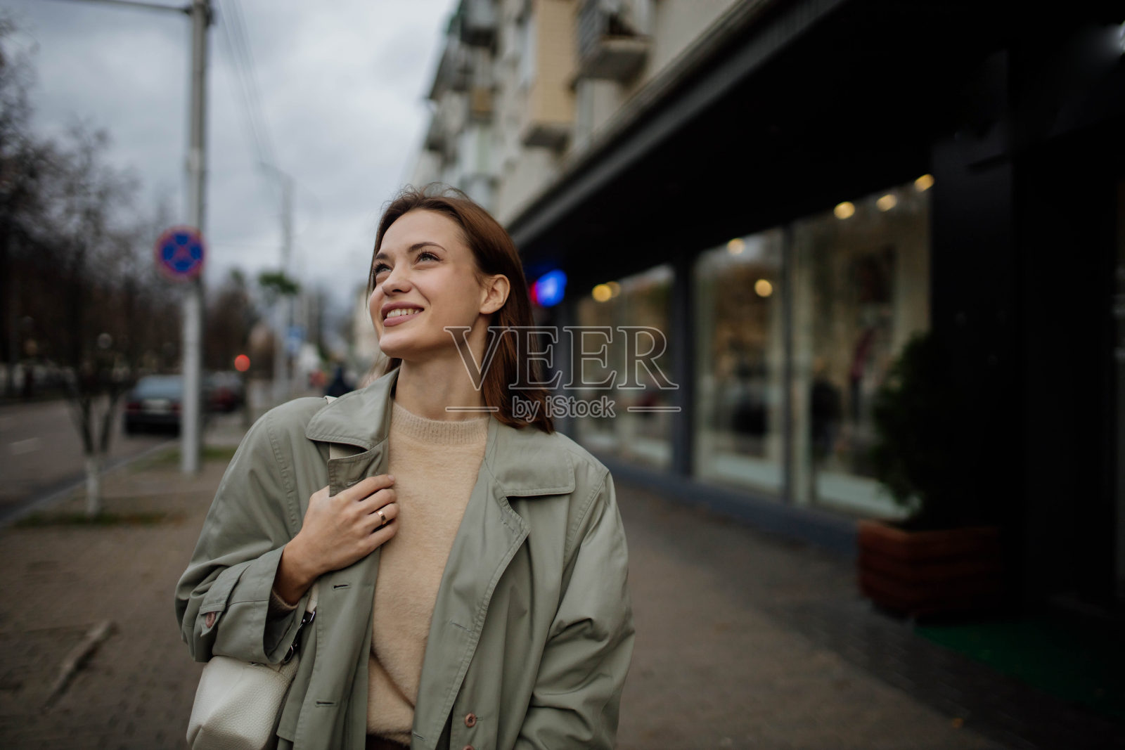 春天里，一个美丽、开朗的女人穿着一件灰色外套在商店附近的城市里走来走去照片摄影图片
