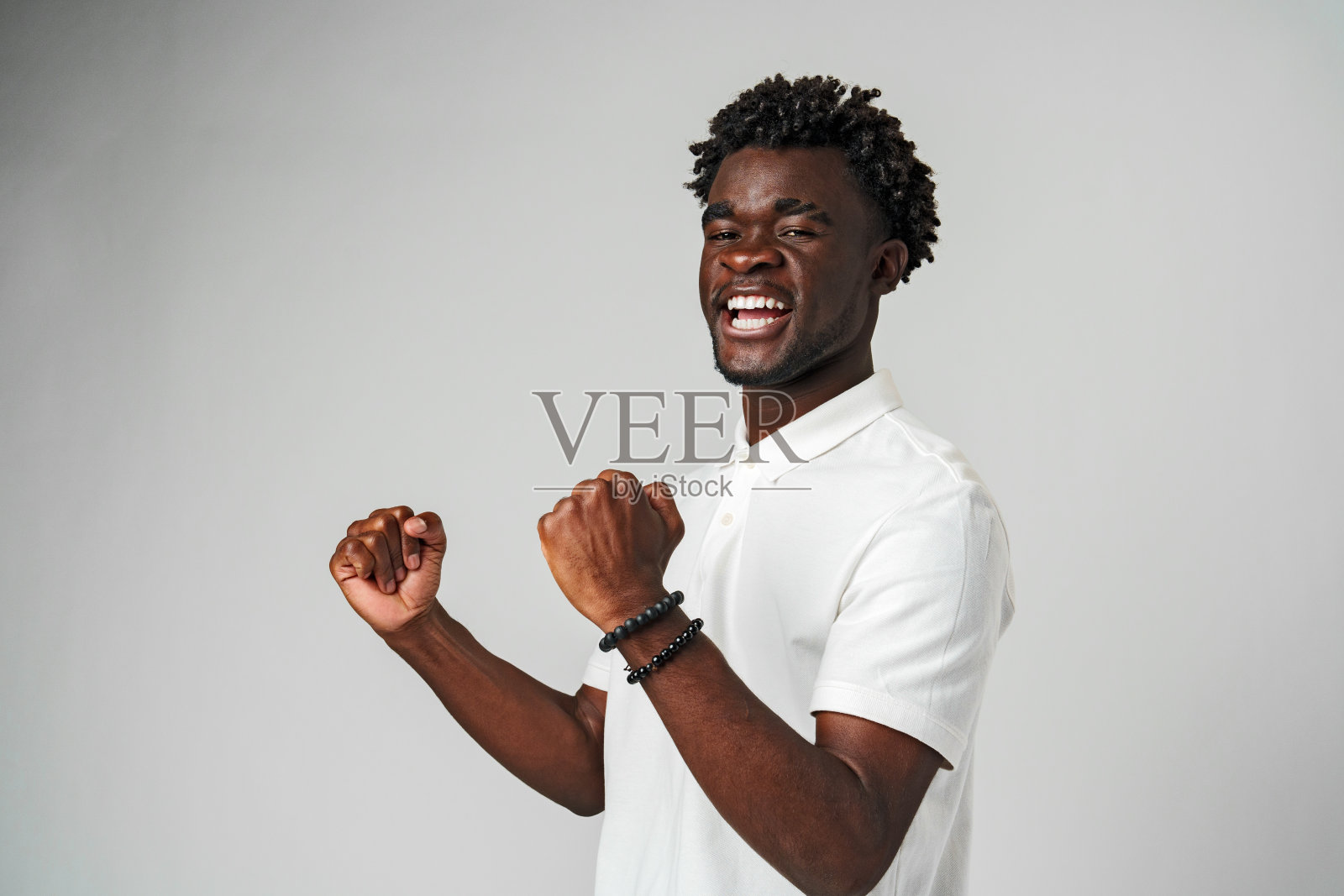 穿着白色Polo衫的微笑年轻人在室内高举拳头庆祝照片摄影图片