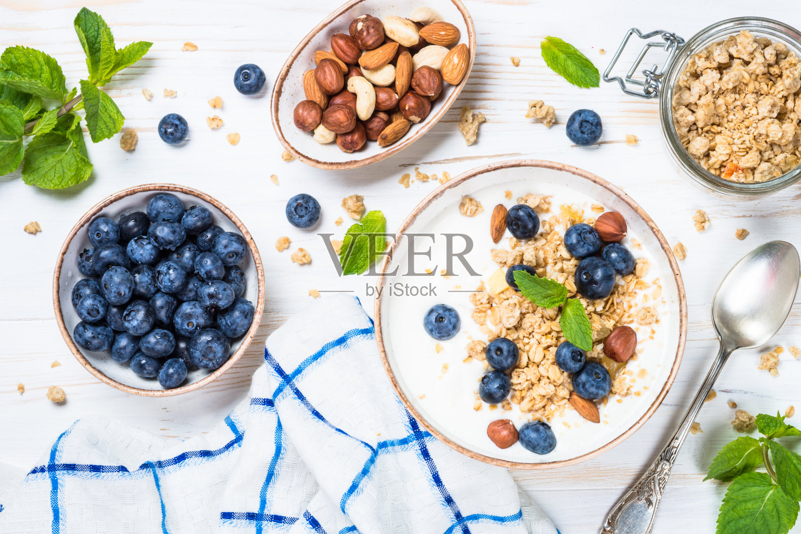 白色木桌上的酸奶格兰诺拉麦片配新鲜蓝莓。照片摄影图片