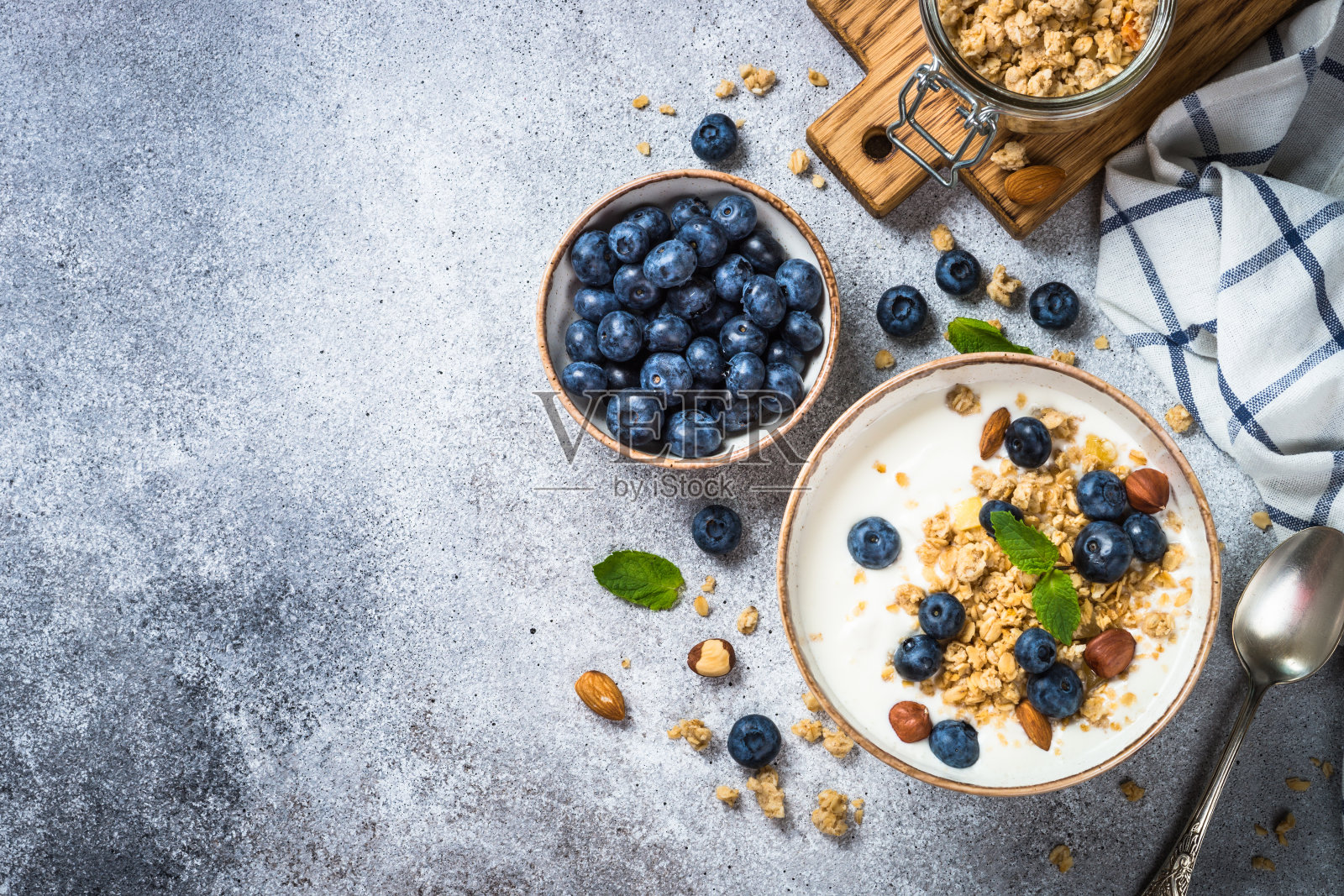 石桌上放着酸奶格兰诺拉麦片和新鲜蓝莓。照片摄影图片