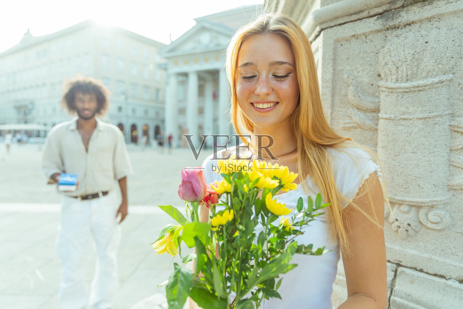 快乐的女人拿着一束鲜花，她的伴侣在身后拿着一个装有戒指的盒子正要求婚照片摄影图片