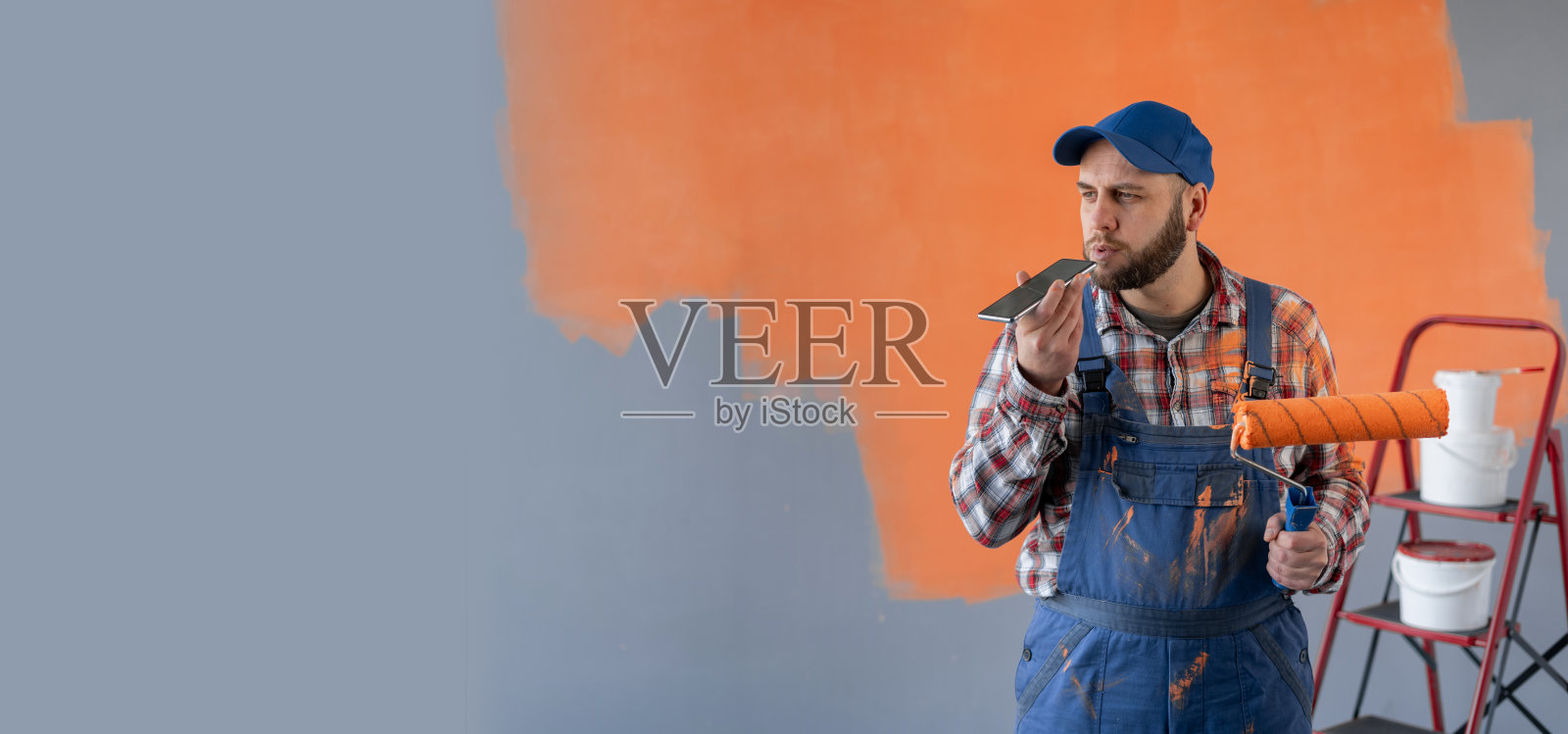 一名油漆工利用智能手机在线语音识别，站在家里的房间里进行装修和粉刷墙壁照片摄影图片