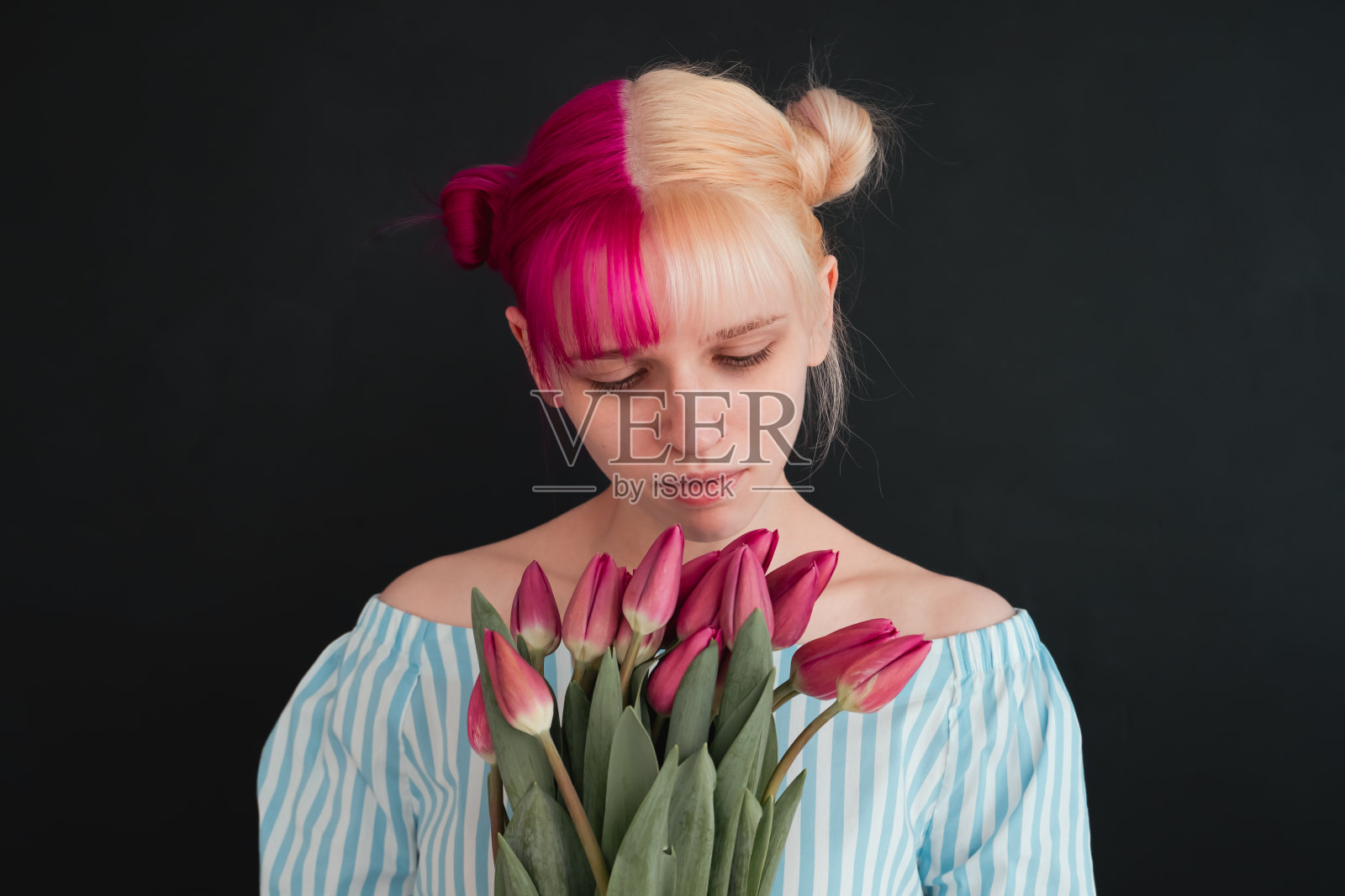 粉色头发的年轻女子在黑色背景下嗅着郁金香花照片摄影图片