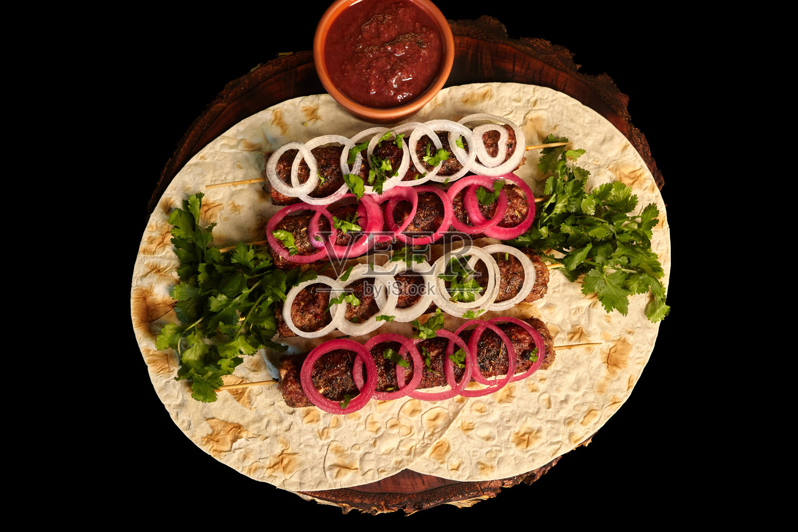 烤肉串:把烤香肠串在肉末上，配上皮塔饼和烧烤酱，再用腌洋葱装饰在木板上。东方美食。前视图。照片摄影图片