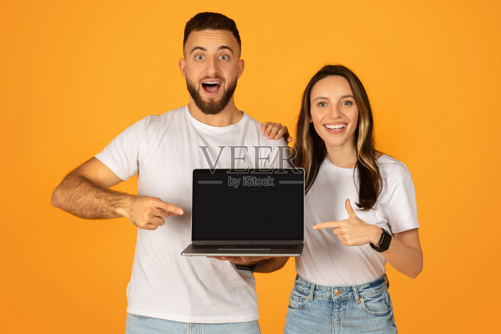兴奋的年轻夫妇展示了一台空白屏幕的笔记本电脑，非常适合做广告照片摄影图片