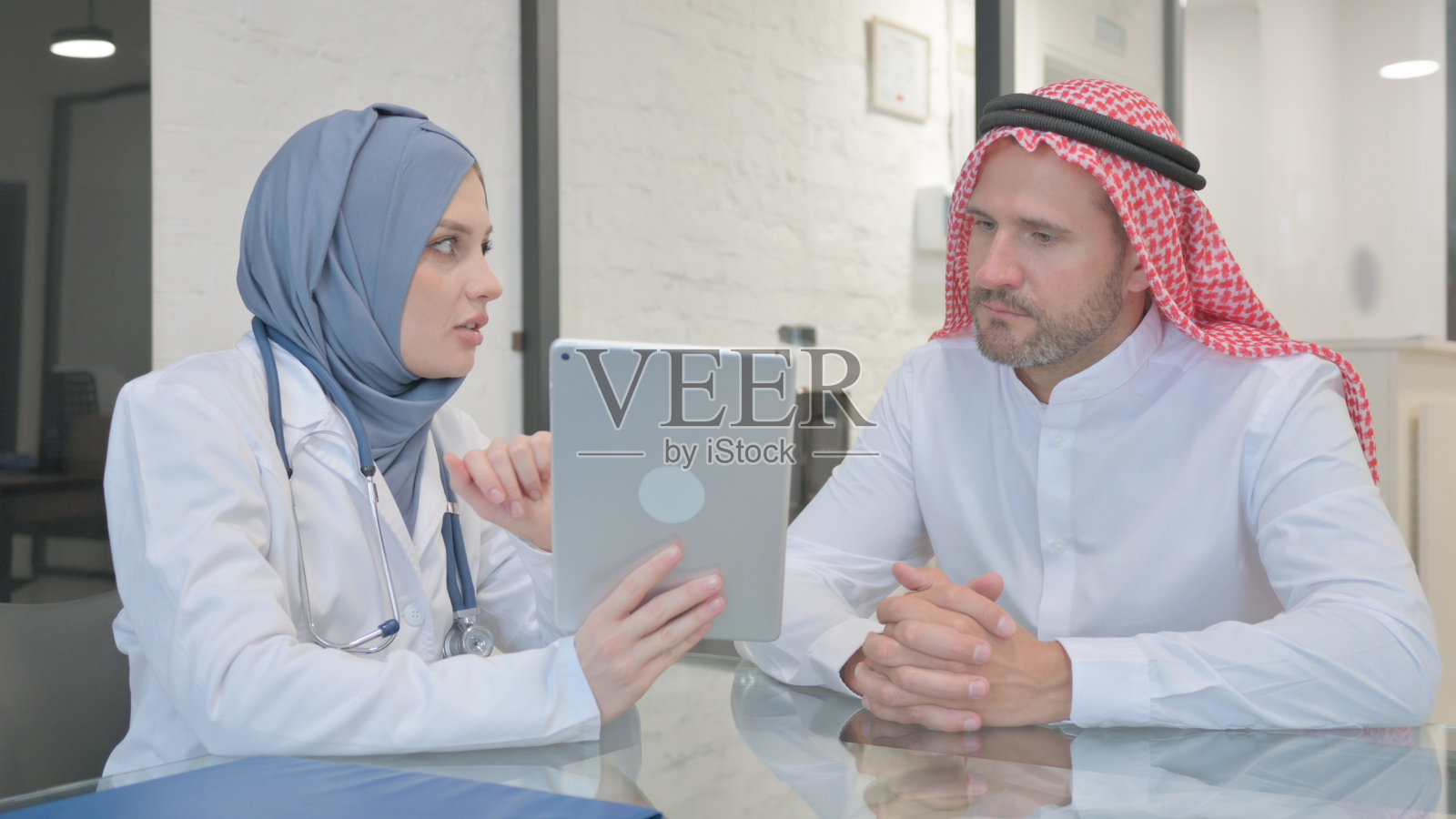 戴头巾的医生在电子平板电脑上与病人讨论治疗照片摄影图片