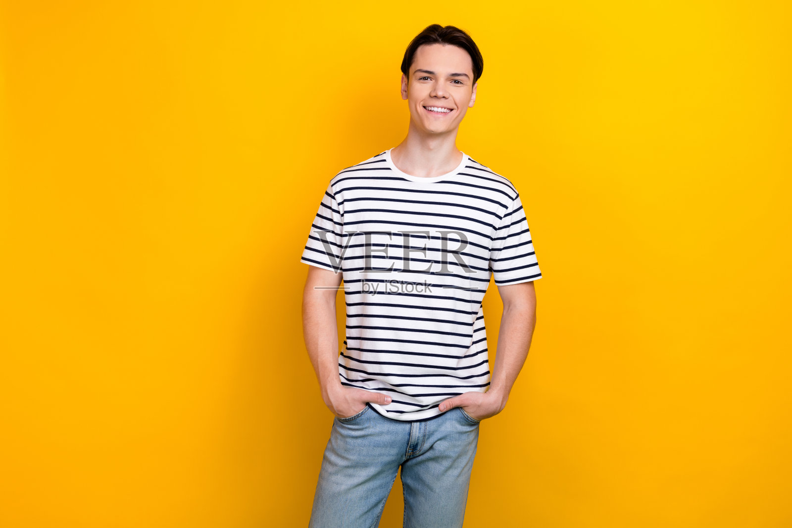 照片中，一个留着时髦发型、穿着条纹t恤、自信十足的男孩，双手放在口袋里，背景是鲜艳的黄色照片摄影图片