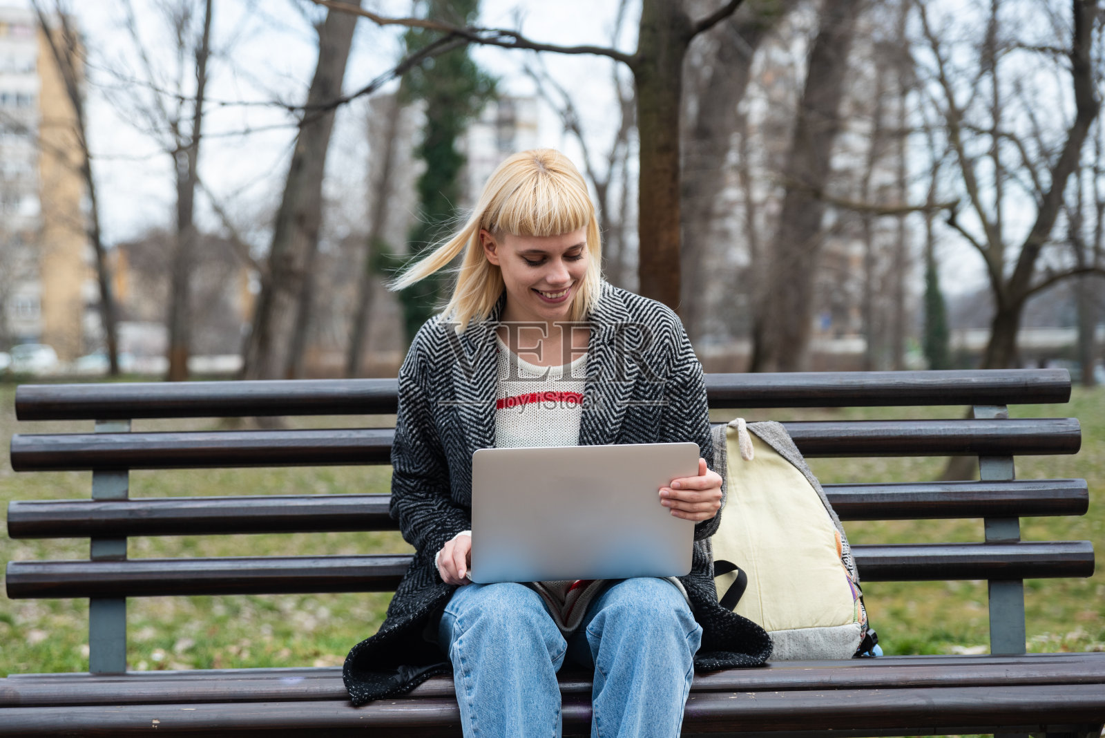 年轻成功的时髦女商人Z一代坐在公园长椅上用笔记本电脑工作。身着休闲装的专业商务女上班族在办公大楼外调研照片摄影图片