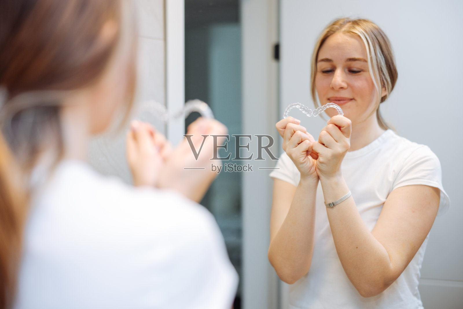 在浴室镜子里取下透明固位器的女人照片摄影图片