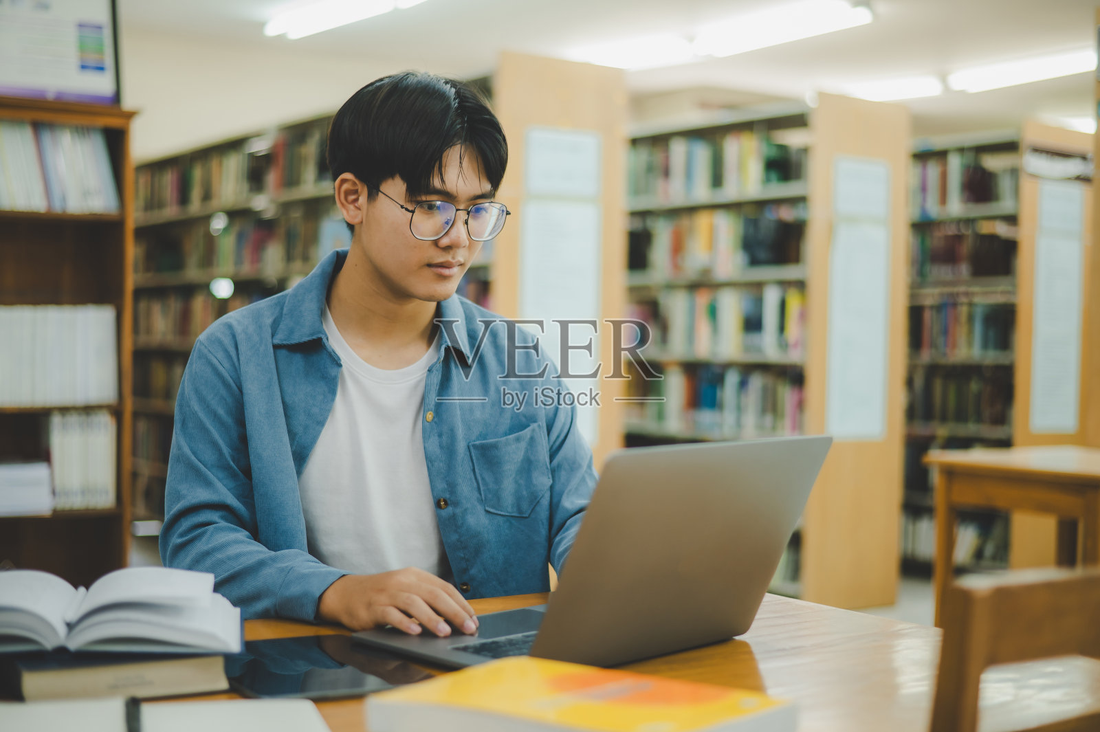 男大学生在笔记本电脑上工作，寻找书籍学习，做报告，在大学房间里找到有用的信息。读书、学习、智慧的概念。照片摄影图片