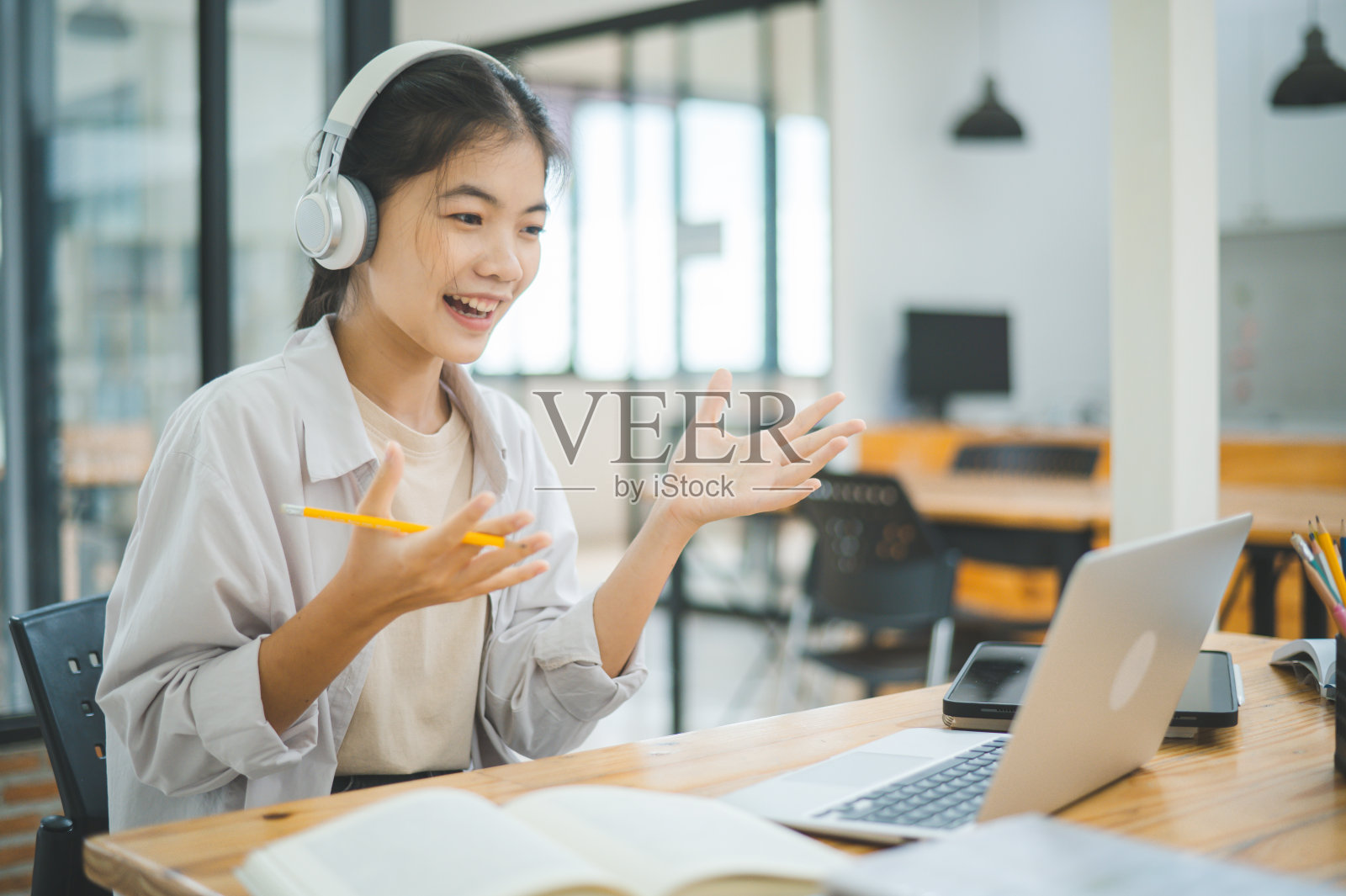 十几岁的亚洲学生戴着耳机，通过视频会议进行在线学习。通过应用进行视频电话会议。照片摄影图片