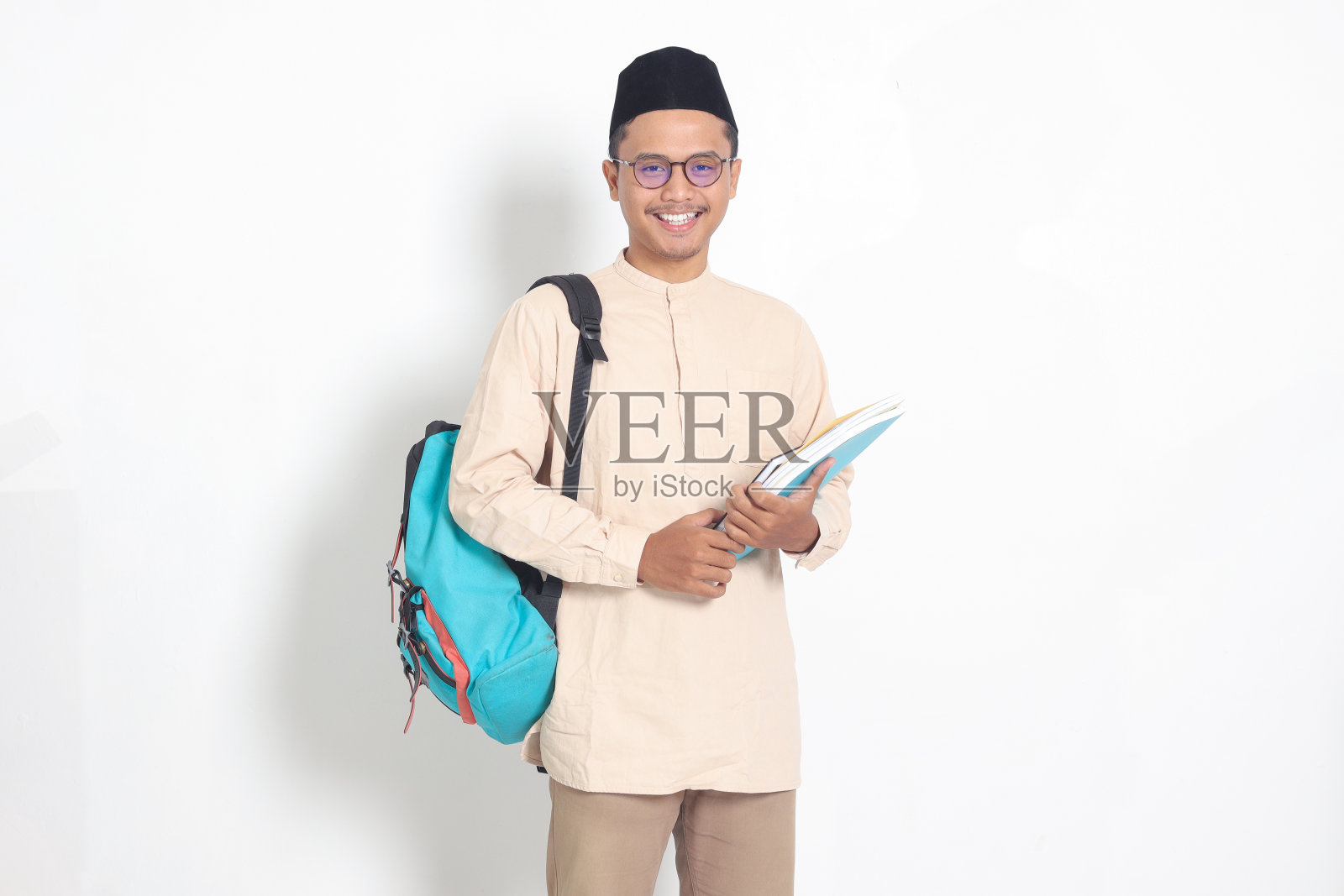 戴着小帽、穿着koko衬衫、背着书包的穆斯林男学生兴奋的肖像照片摄影图片