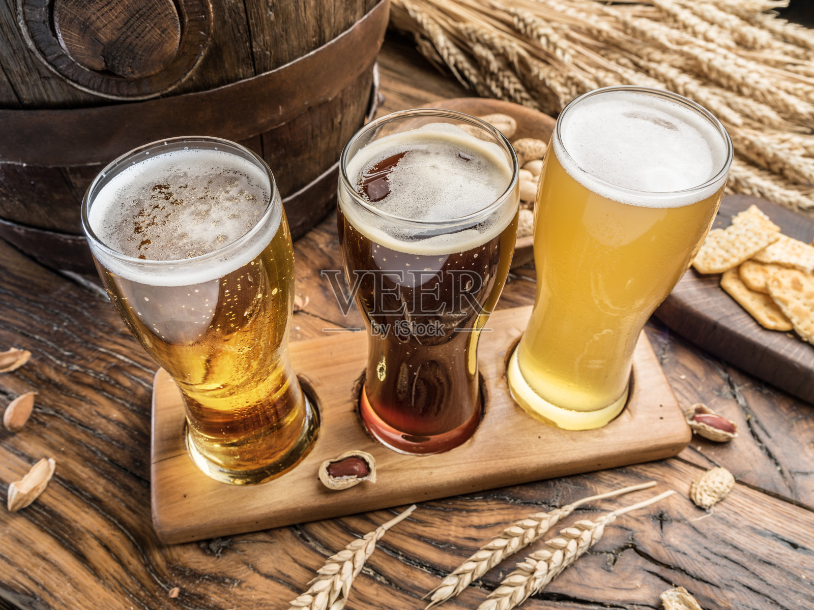 三杯精酿啤酒在木制啤酒飞行板上。背景是啤酒杯、小吃和啤酒桶的俯视图。照片摄影图片
