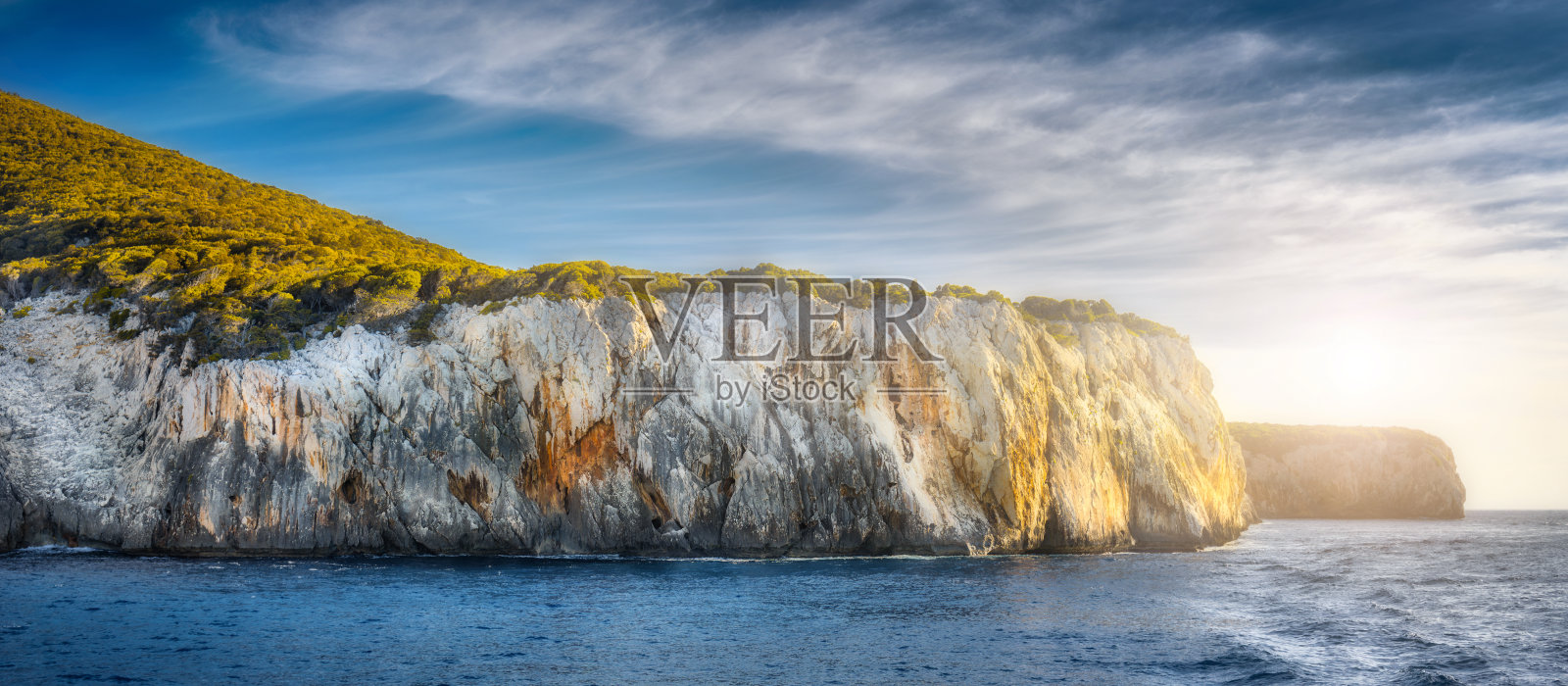 夏天的海景观，悬崖覆盖了绿色的树木在日落的晴天照片摄影图片