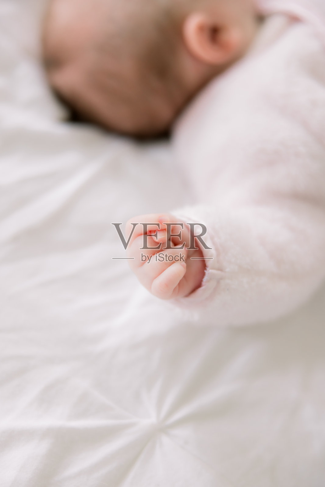 可爱的新生儿躺在床上，小手握在拳头里。照片摄影图片