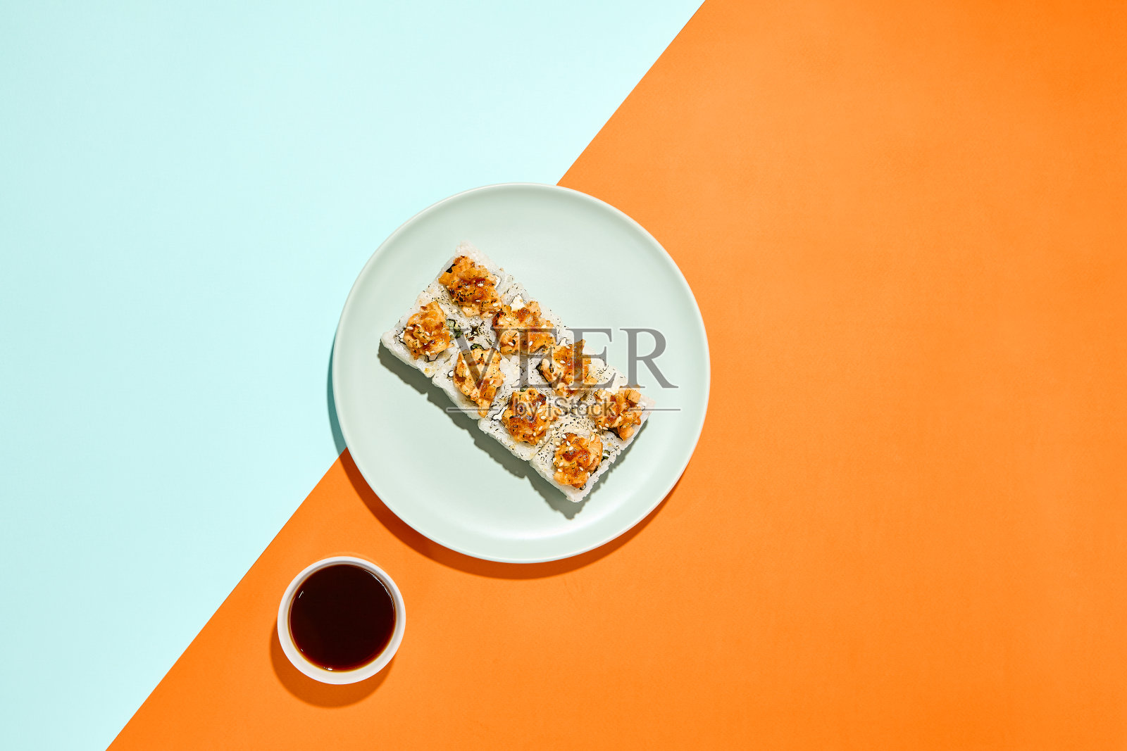 在彩色背景的陶瓷盘子里烤真寿司。时尚风格的鞑靼虾寿司卷，以橙色和蓝色为背景，简约风格的硬阴影寿司卷照片摄影图片