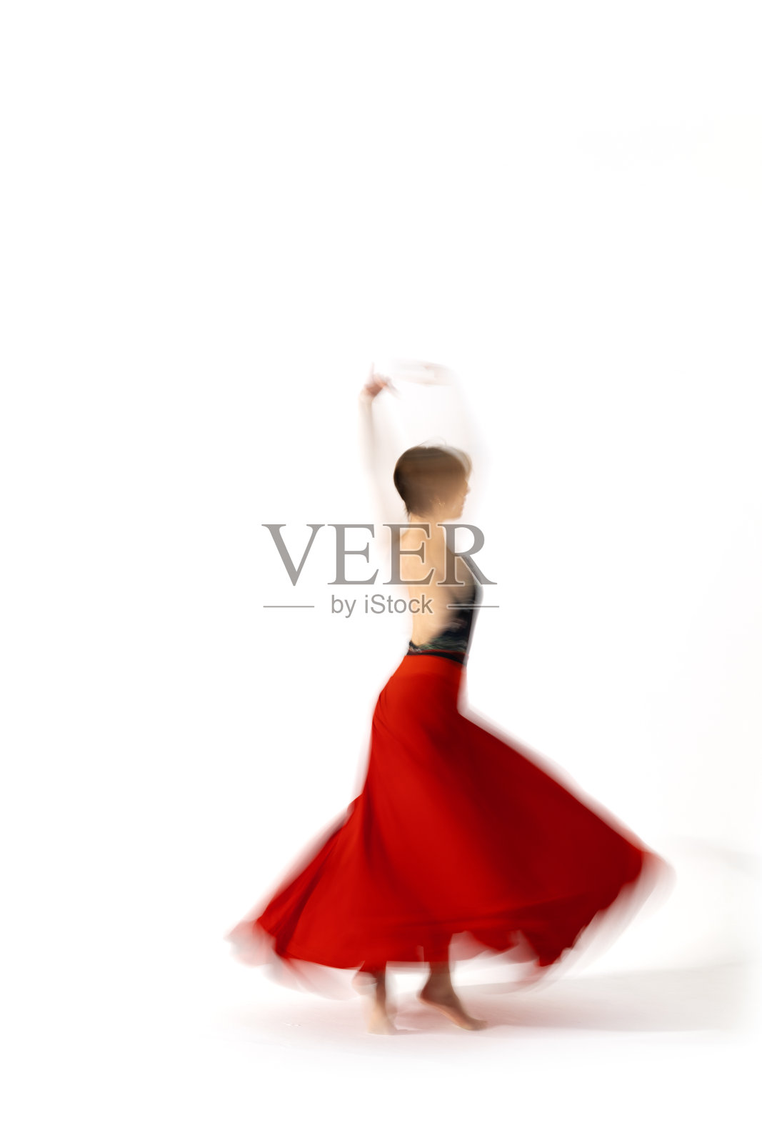 穿着红裙子的年轻芭蕾舞女演员在舞蹈室的灯光下跳舞。长时间的曝光。白色背景照片摄影图片
