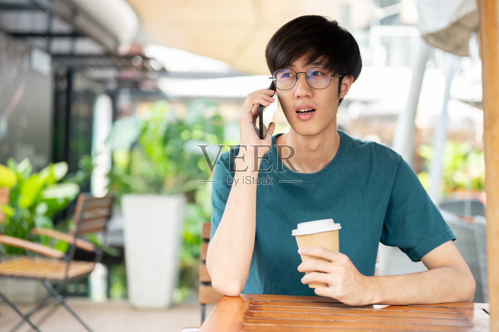 一名男子坐在城市一家咖啡馆的户外桌子上与人通话。照片摄影图片