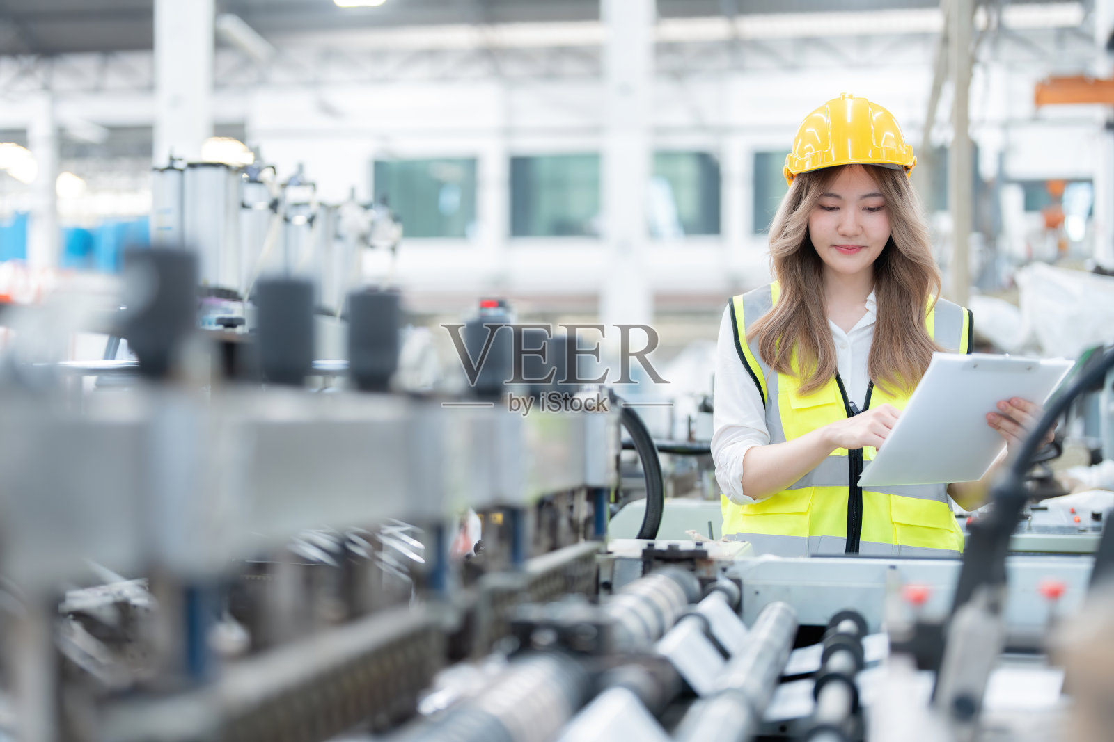 一位知识渊博的亚洲女工程师的作品是一家工业公司的负责人，该公司在欧洲的一家工厂生产汽车和具有现代和复杂机械的机器人。照片摄影图片