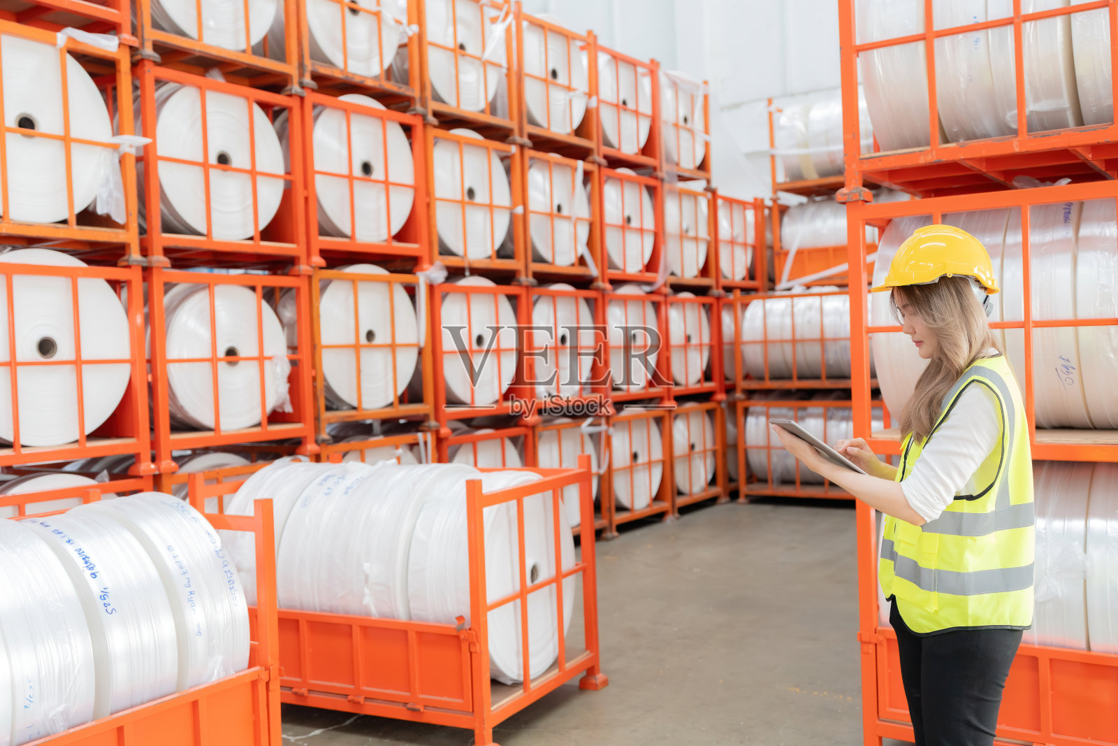 一家大型工业工厂有多个架子的钢架纸卷等待出口生产。质量和标准由一名带着笔记本电脑的亚洲女工程师检查。照片摄影图片