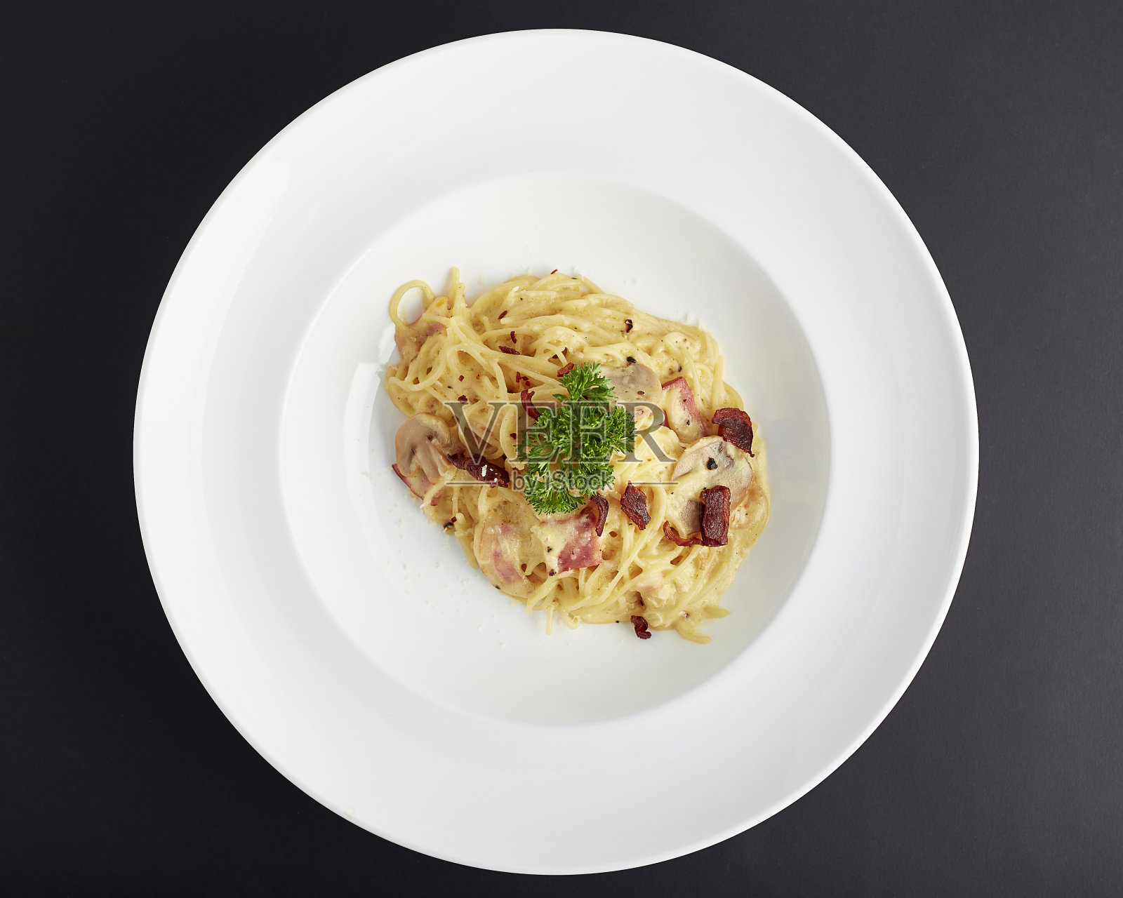 上图为火腿、培根、蘑菇片和迷迭香叶的意大利面条，装在白色盘子里，背景是黑色的。意大利菜。照片摄影图片