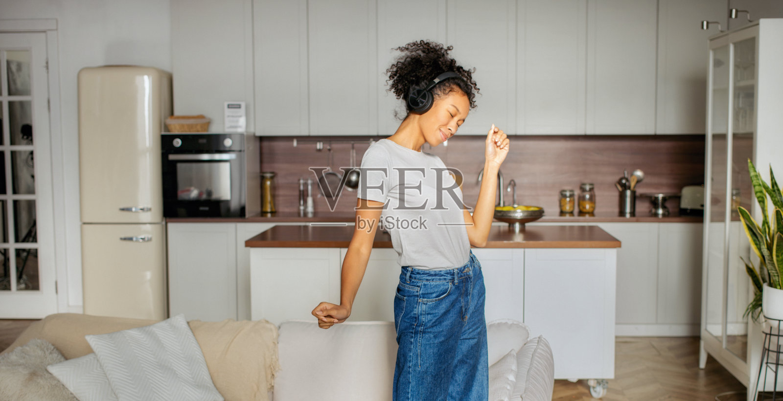 快乐的女人戴着耳机在厨房里快乐地跳舞，享受着家中的悠闲照片摄影图片
