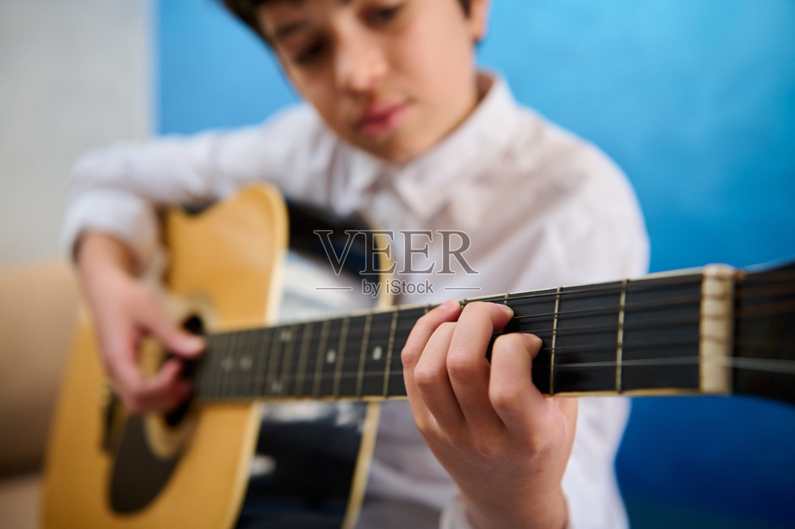 在音乐课上，十几岁的男孩吉他手在弹原声吉他时拨弦的细节。爱好与休闲照片摄影图片