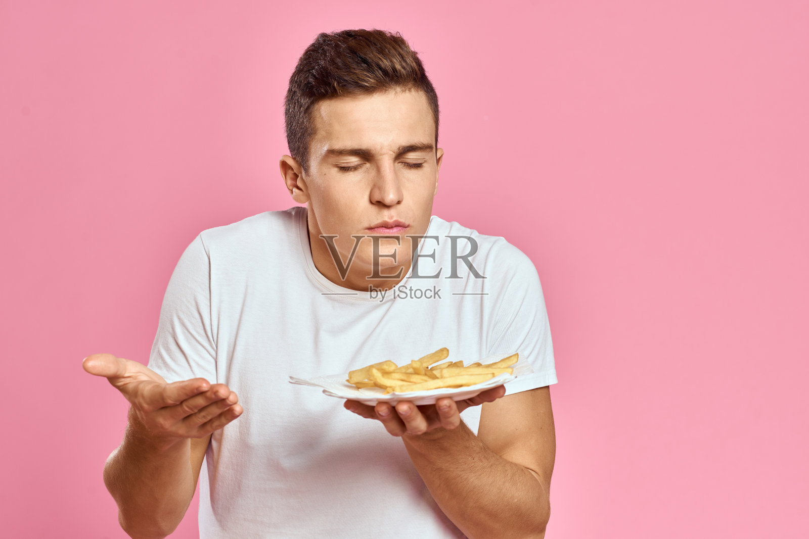 男子与薯条在一个纸盒上的粉红色背景卡路里快餐肖像粉红色背景照片摄影图片