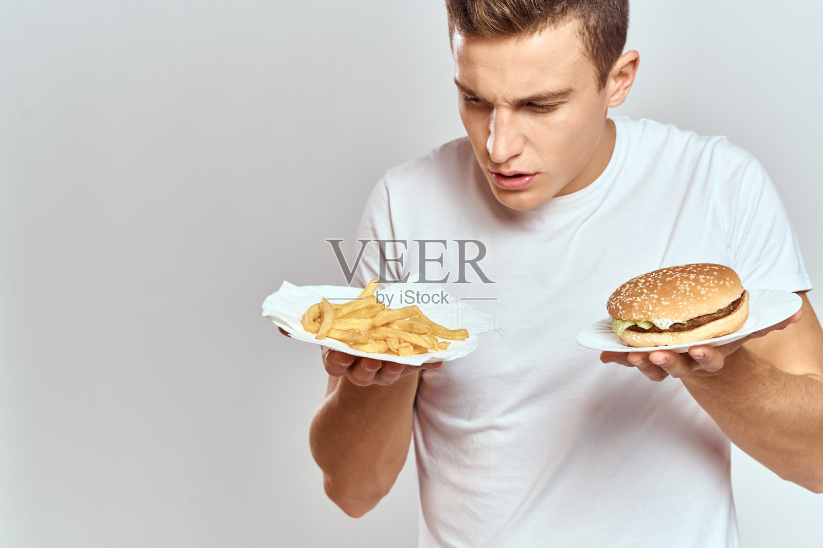 一个穿着白色t恤的男人拿着薯条和汉堡包在浅色背景上照片摄影图片