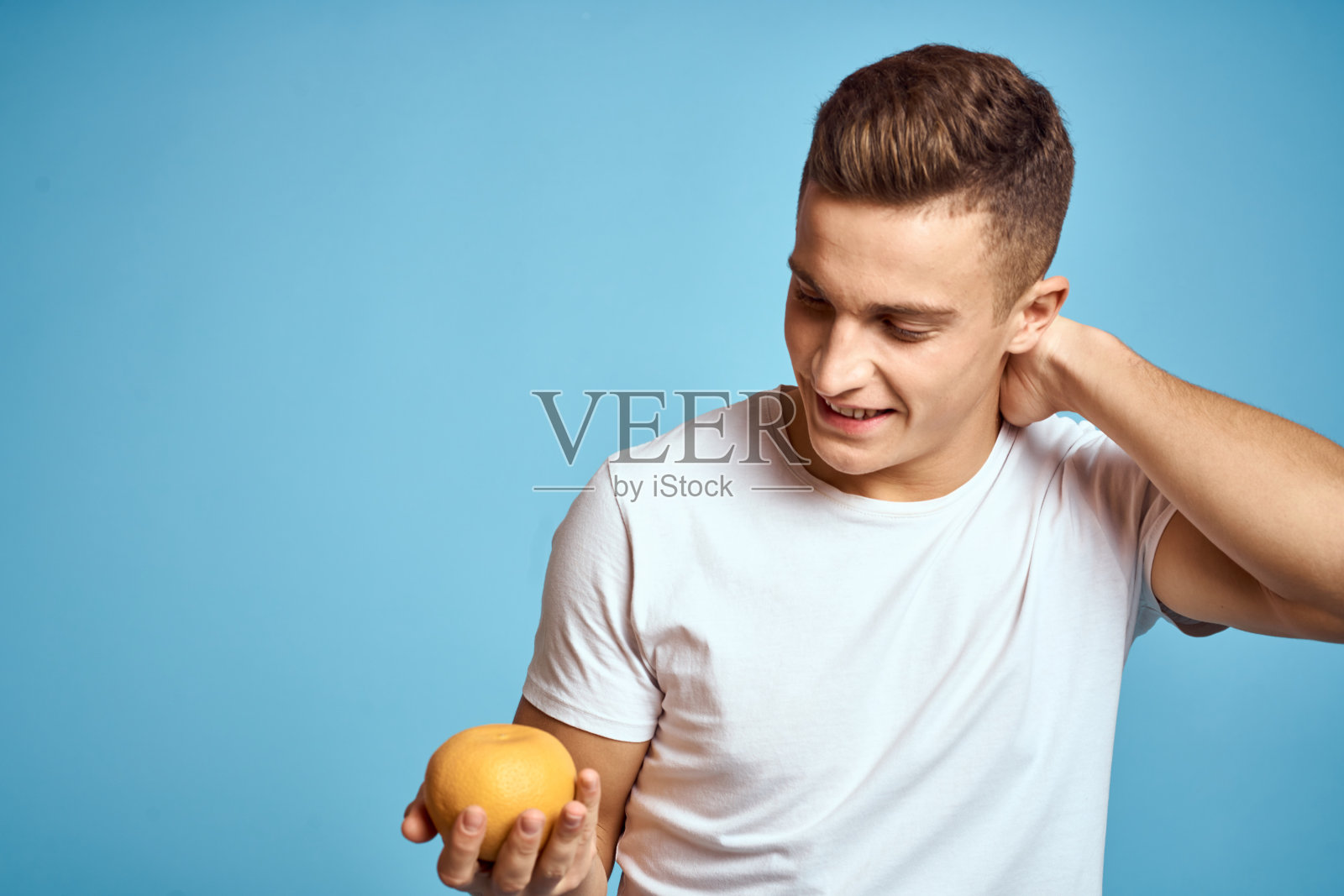 快乐的男人拿着新鲜的水果用手比画蓝色背景白色t恤维他命橙子照片摄影图片