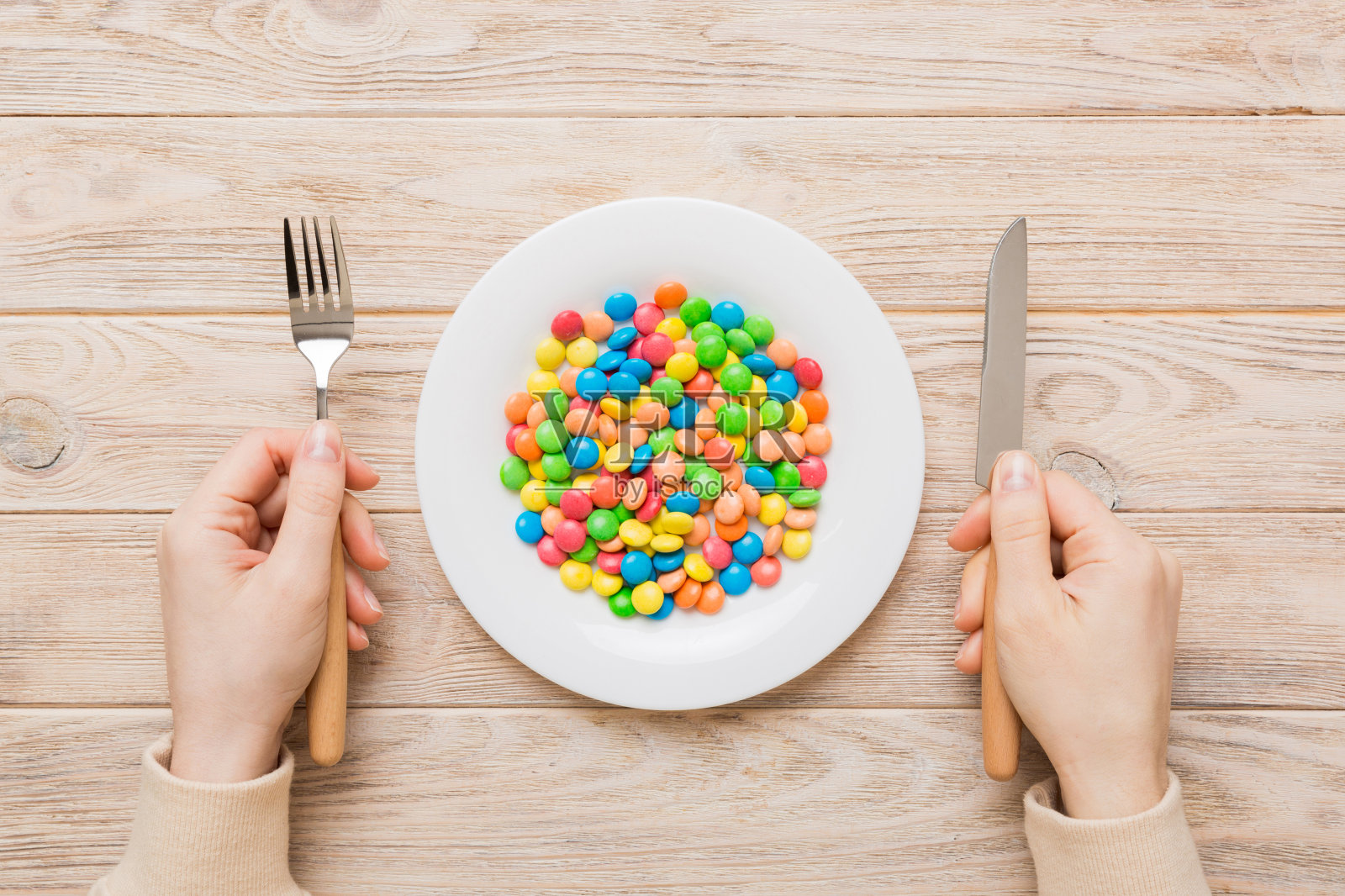 这个女孩手里拿着餐具，吃着盘子里的糖果。健康与肥胖概念，彩色背景俯视图照片摄影图片