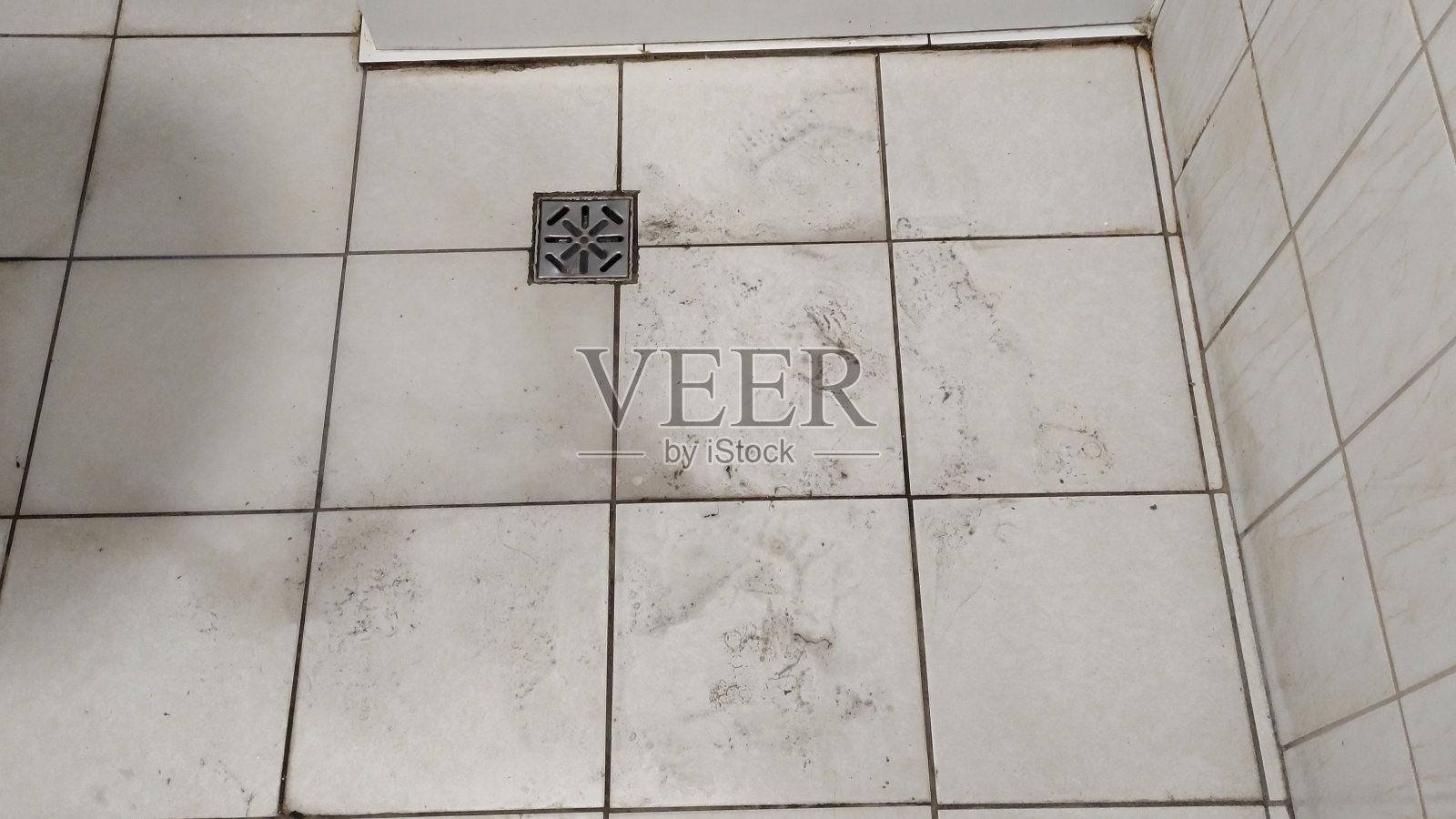 在廉价旅馆或学生宿舍里，又旧又脏的瓷砖浴室里有淋浴，肮脏的地板上有鞋子的痕迹照片摄影图片