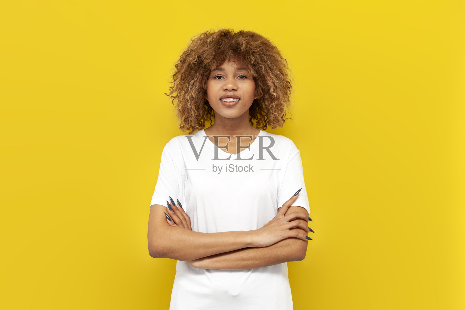 穿着白色t恤的严肃卷发的非洲裔美国女孩站在黄色孤立的背景上，双臂交叉照片摄影图片